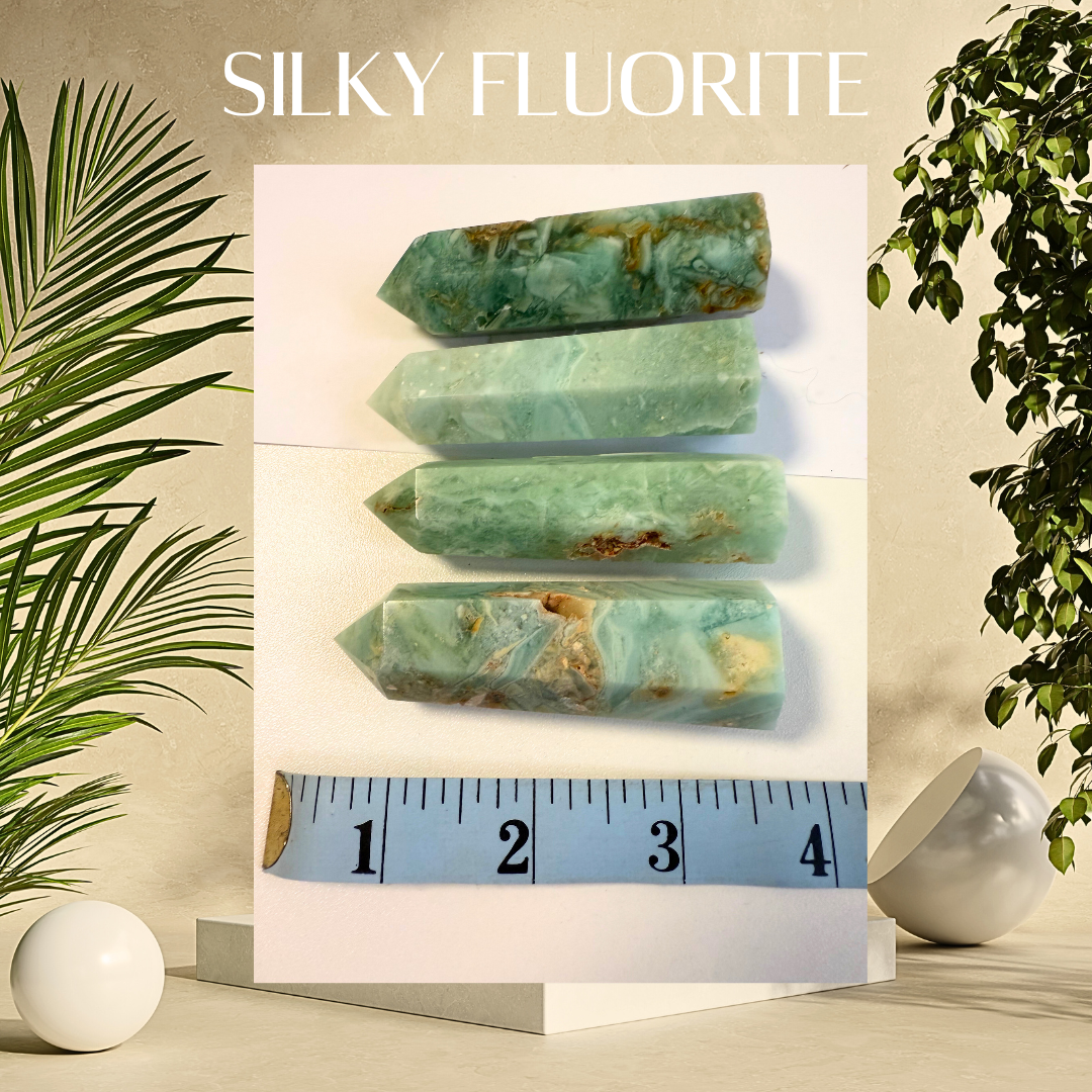 Silky fluorite crystals with a ruler for scale, set against a neutral background with plants.