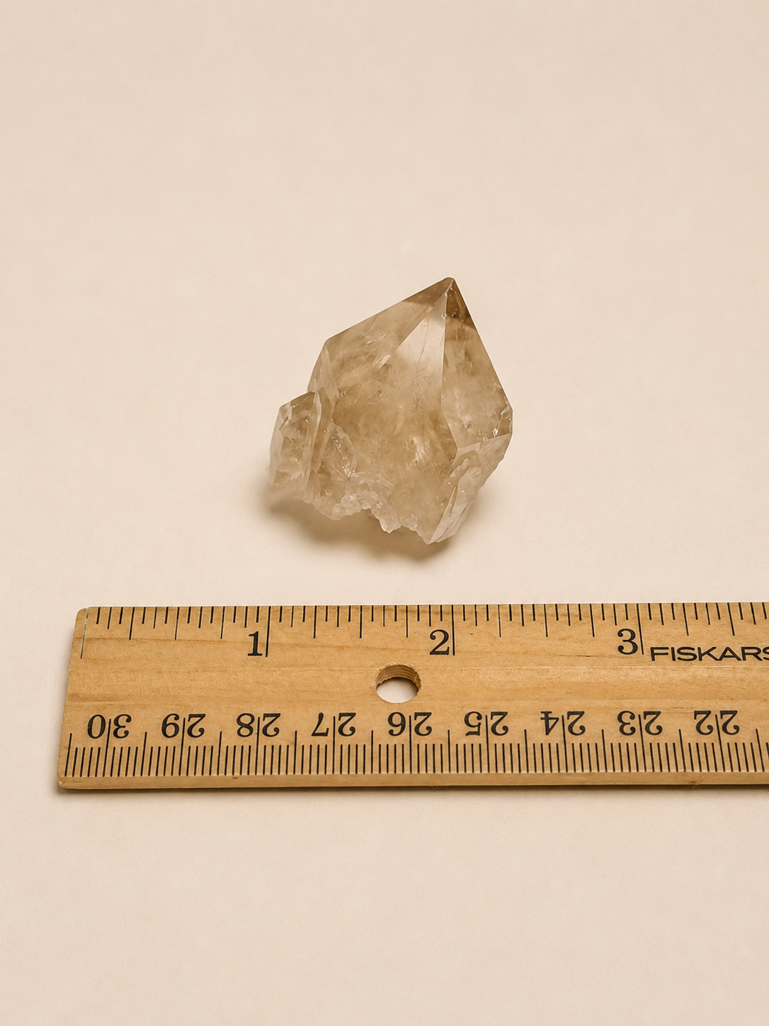 A natural smoky quartz crystal cluster placed above a wooden Fiskars ruler on a plain beige background, showing its size.