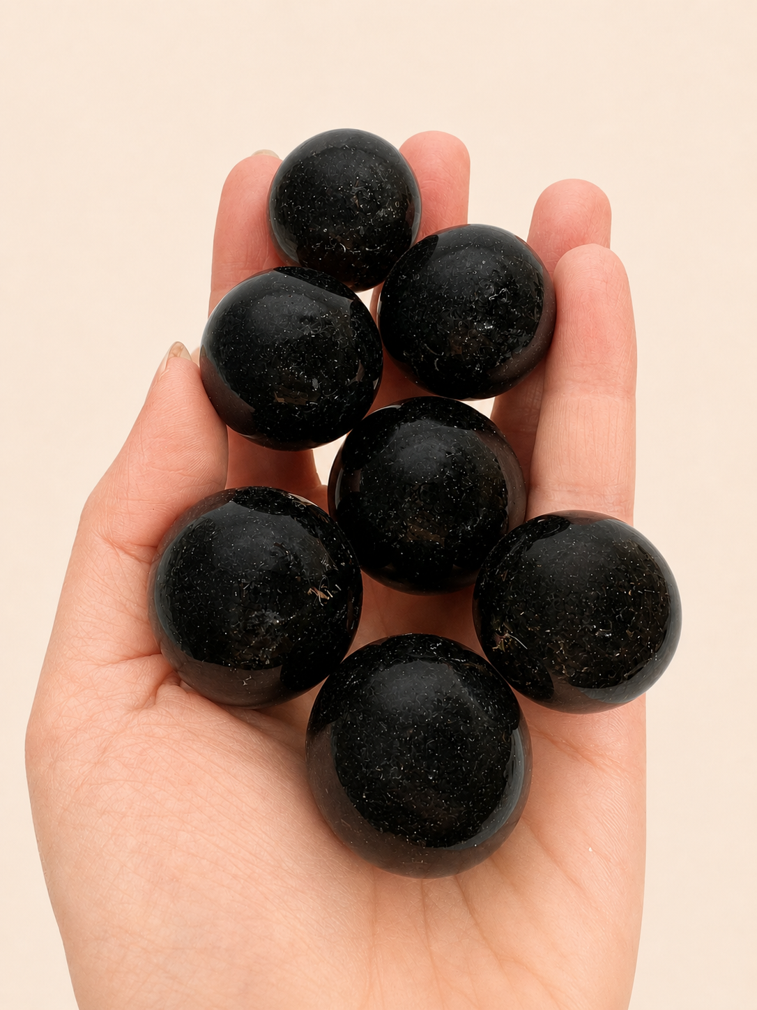 A hand holding seven polished black jasper stone balls against a solid light beige background.