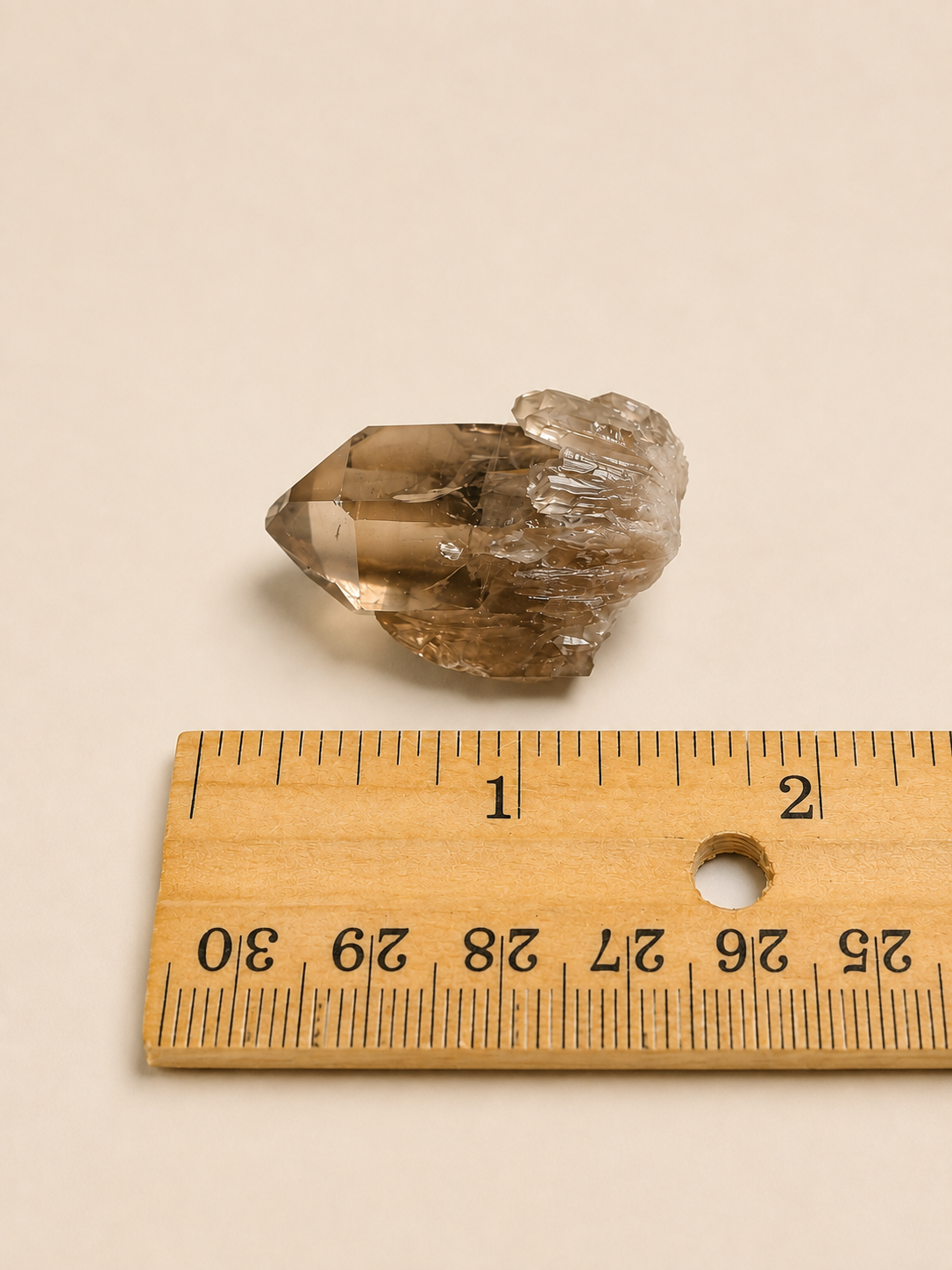 A natural smoky quartz crystal point shown next to a wooden ruler on a plain beige background.