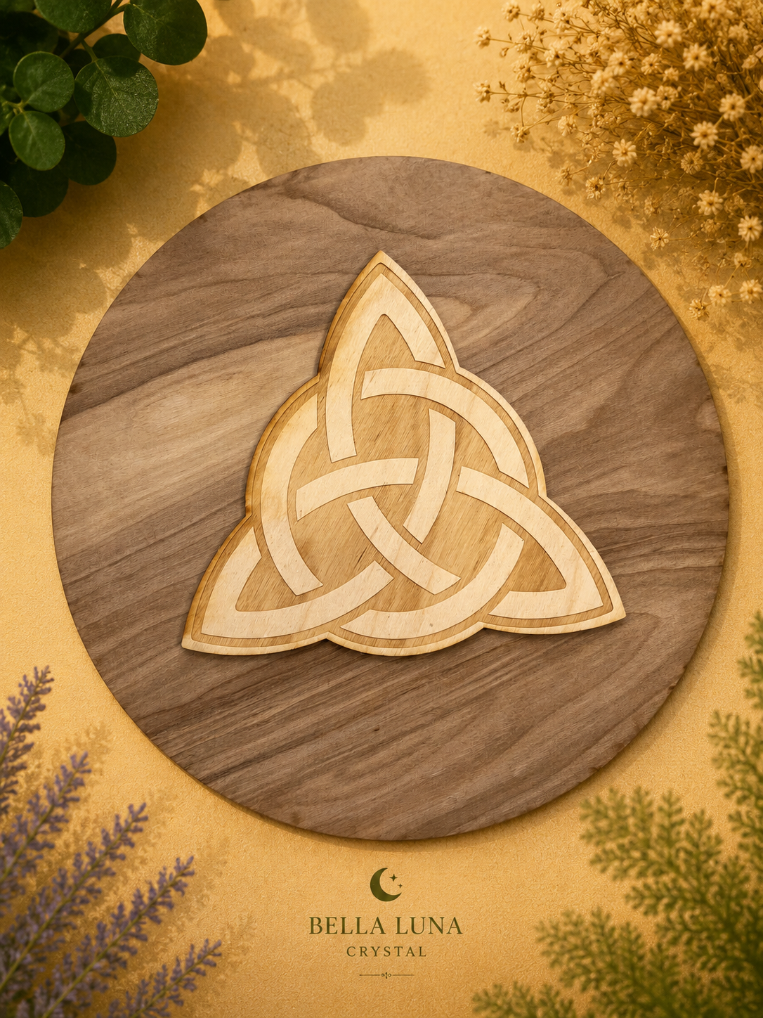 A circular wooden tray or serving board with a natural wood grain finish, featuring a light-colored Celtic triquetra knot design in the center. The board is photographed from above on a textured gold background decorated with dried flowers, green leaves, and lavender sprigs.