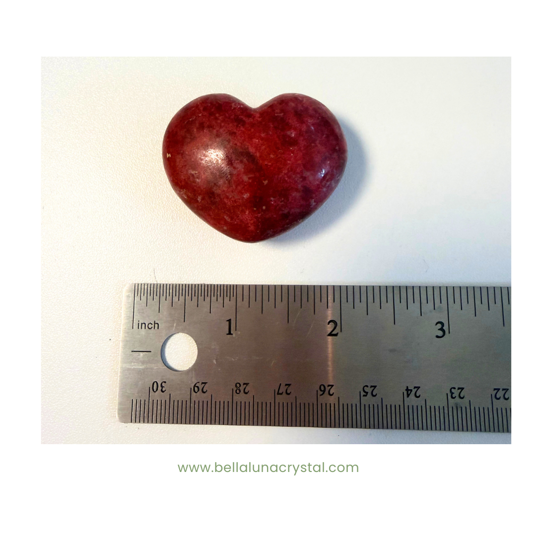 Heart-shaped red stone next to a ruler on a white background