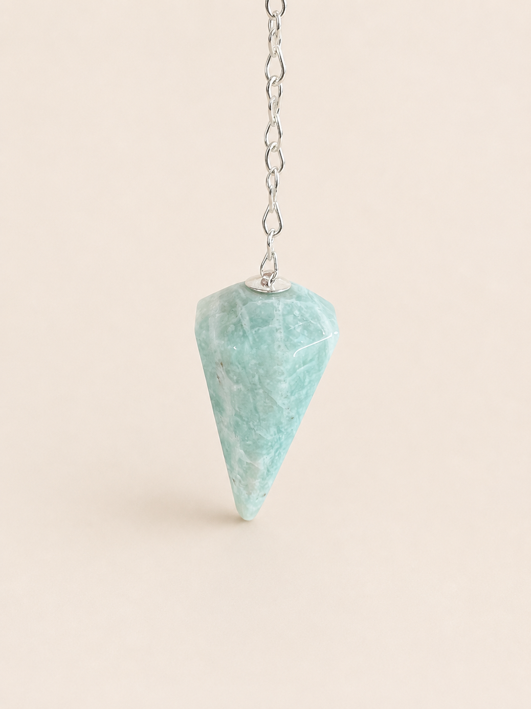 A light blue-green amazonite cone pendant necklace hanging from a silver chain against a solid pale beige background.