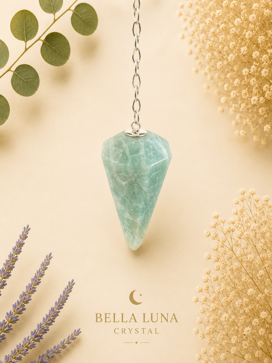 Amazonite crystal pendulum with a silver chain, displayed on a warm beige background with decorative dried flowers and greenery. The brand name 'BELLA LUNA CRYSTAL' is printed at the bottom.