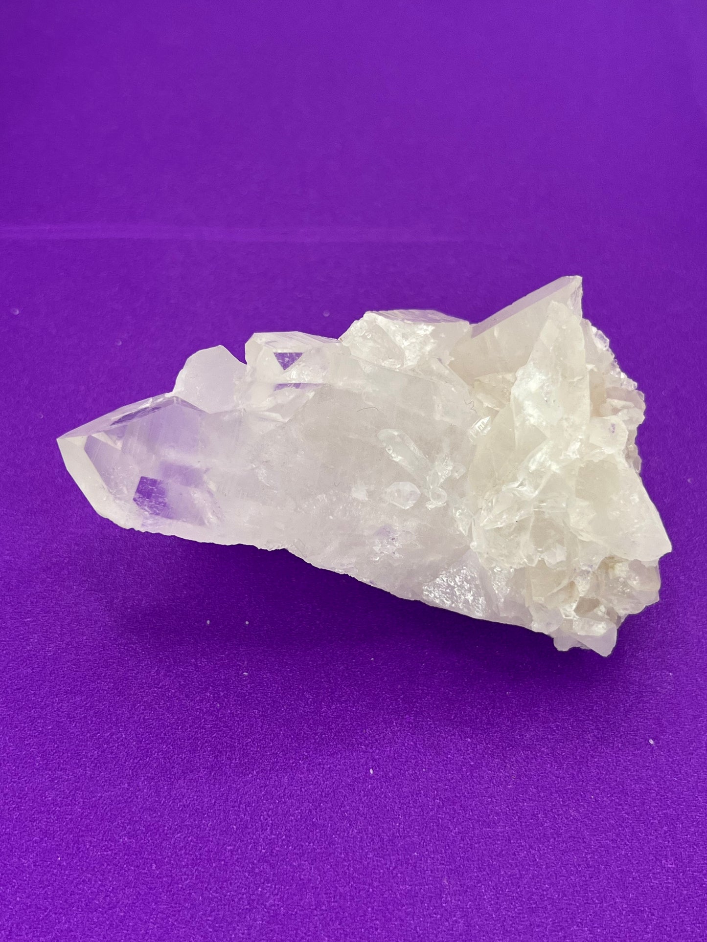 A rough, clear Arkansas quartz crystal cluster on a purple background.