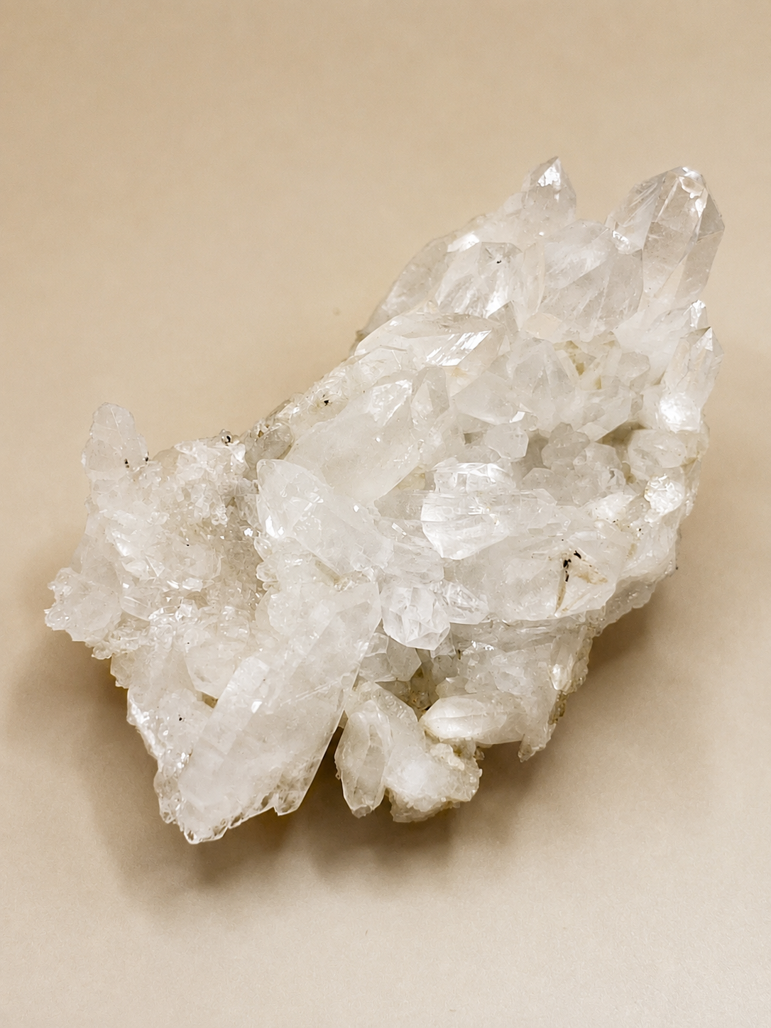 A cluster of clear quartz crystal points on a beige background.