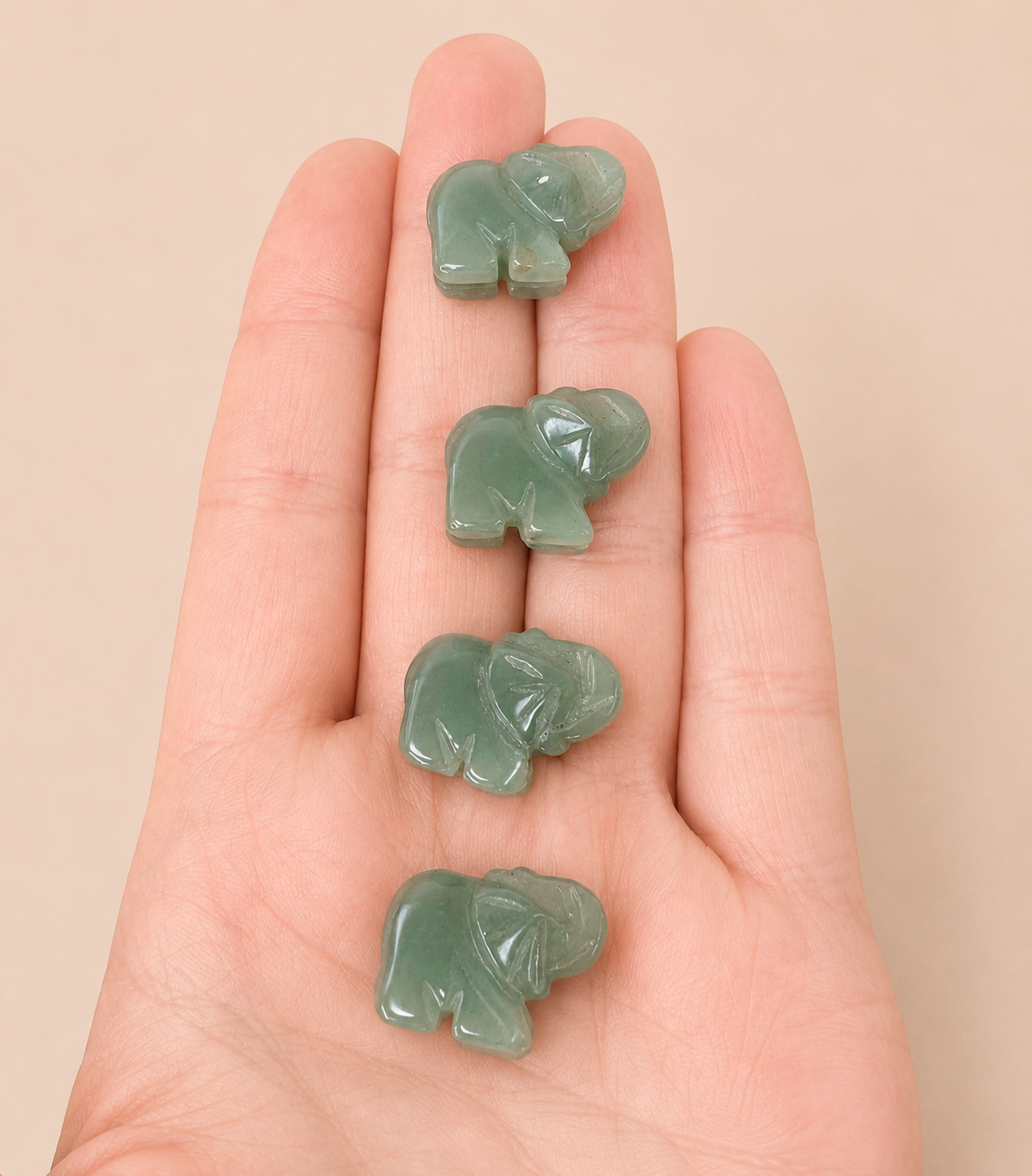 Four small carved green elephant pendants or charms arranged vertically on a person's open hand, against a plain beige background.