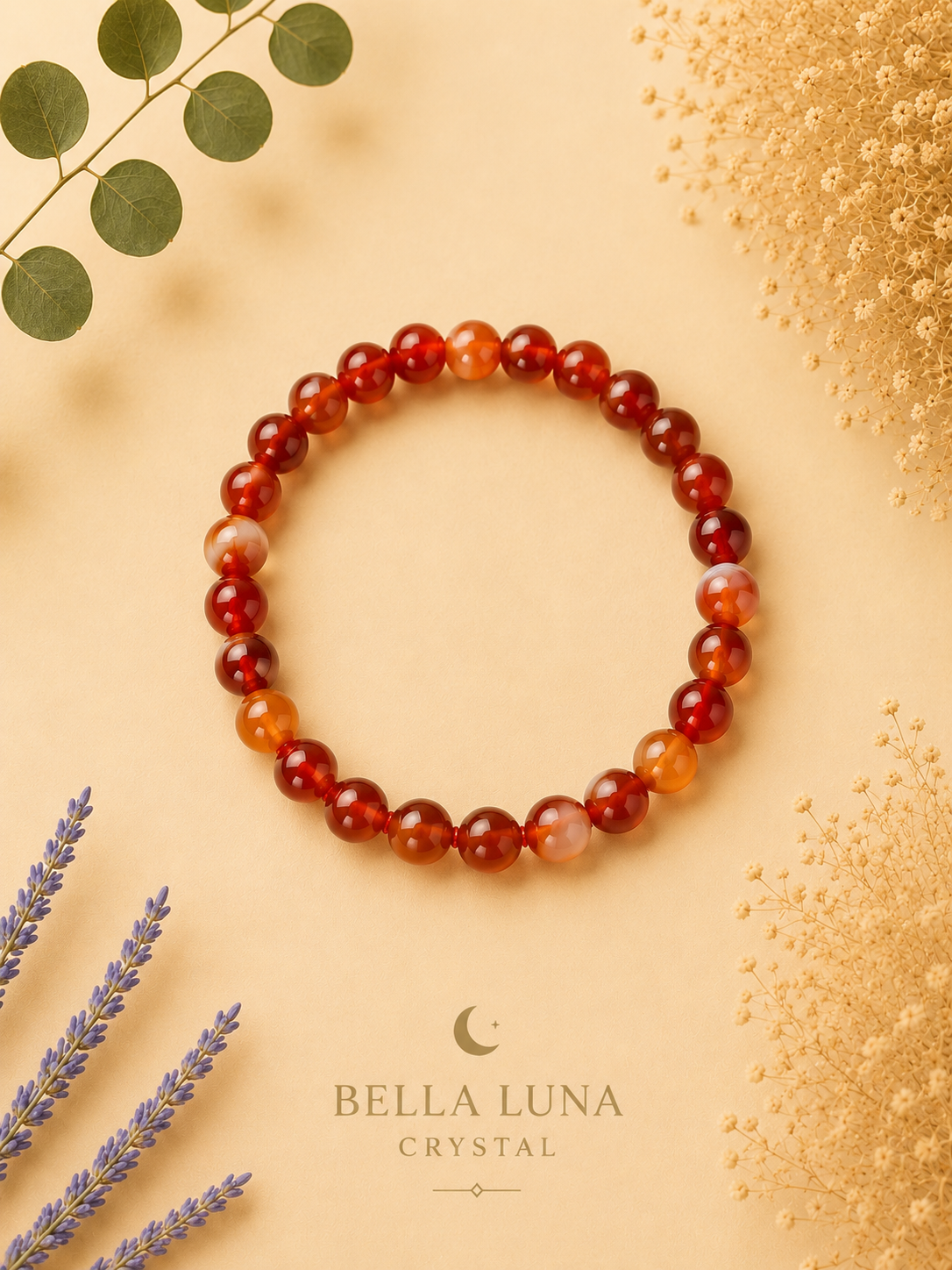 A beaded stretch bracelet made of round red and orange marbled gemstone beads, displayed on a warm beige background with decorative dried flowers, eucalyptus leaves, and lavender sprigs. The brand logo 'BELLA LUNA CRYSTAL' is printed at the bottom.