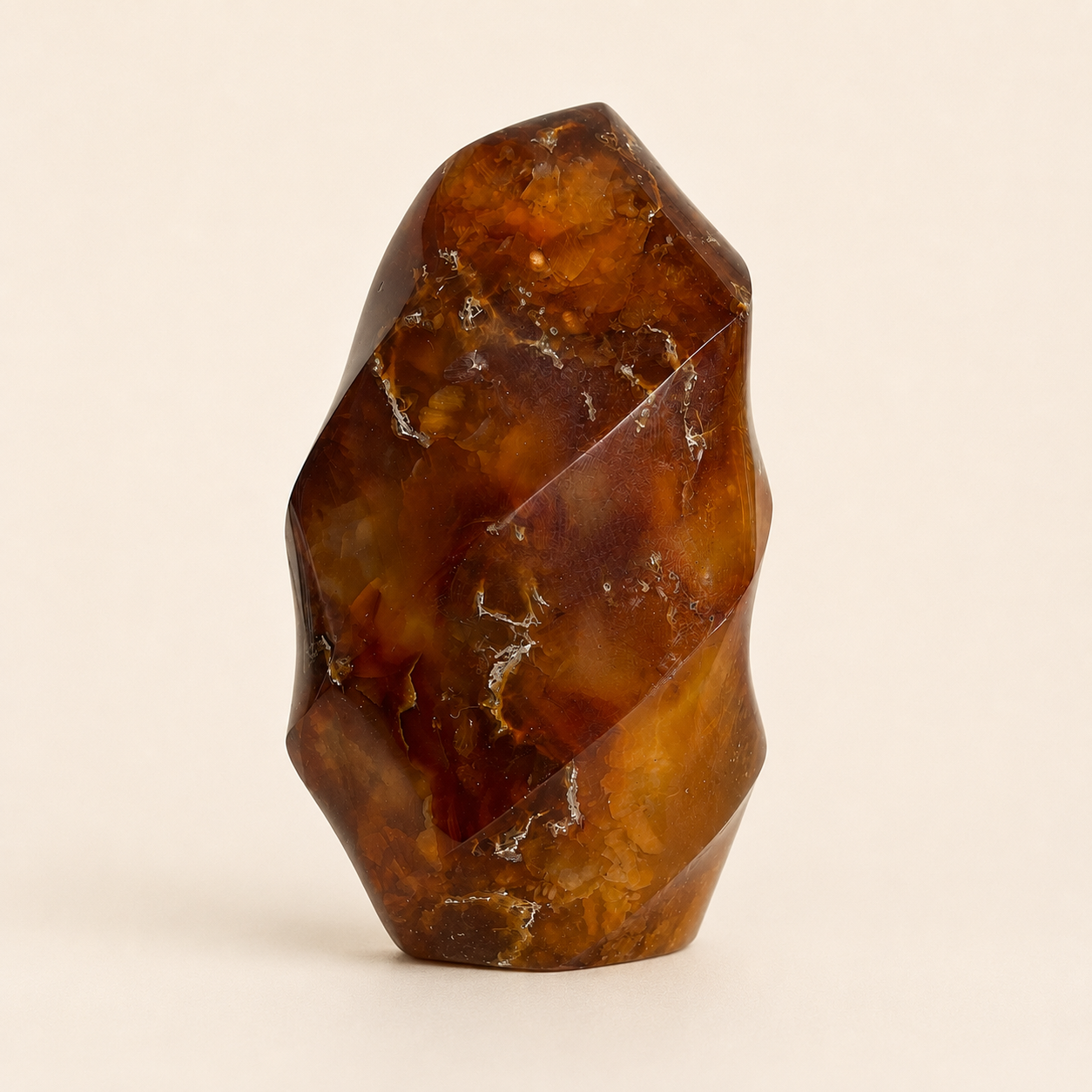 A faceted amber crystal or stone sculpture with a polished, geometric surface, standing upright on a plain beige background.