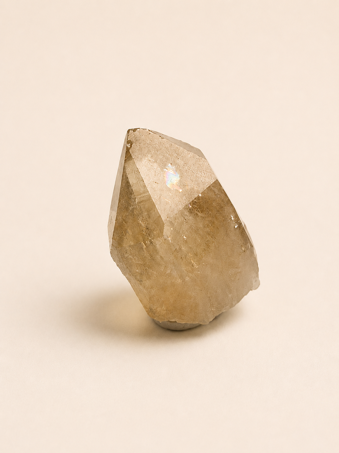 A natural quartz crystal cluster with a pointed tip, showing warm golden-brown and translucent beige tones, photographed on a solid light beige background.