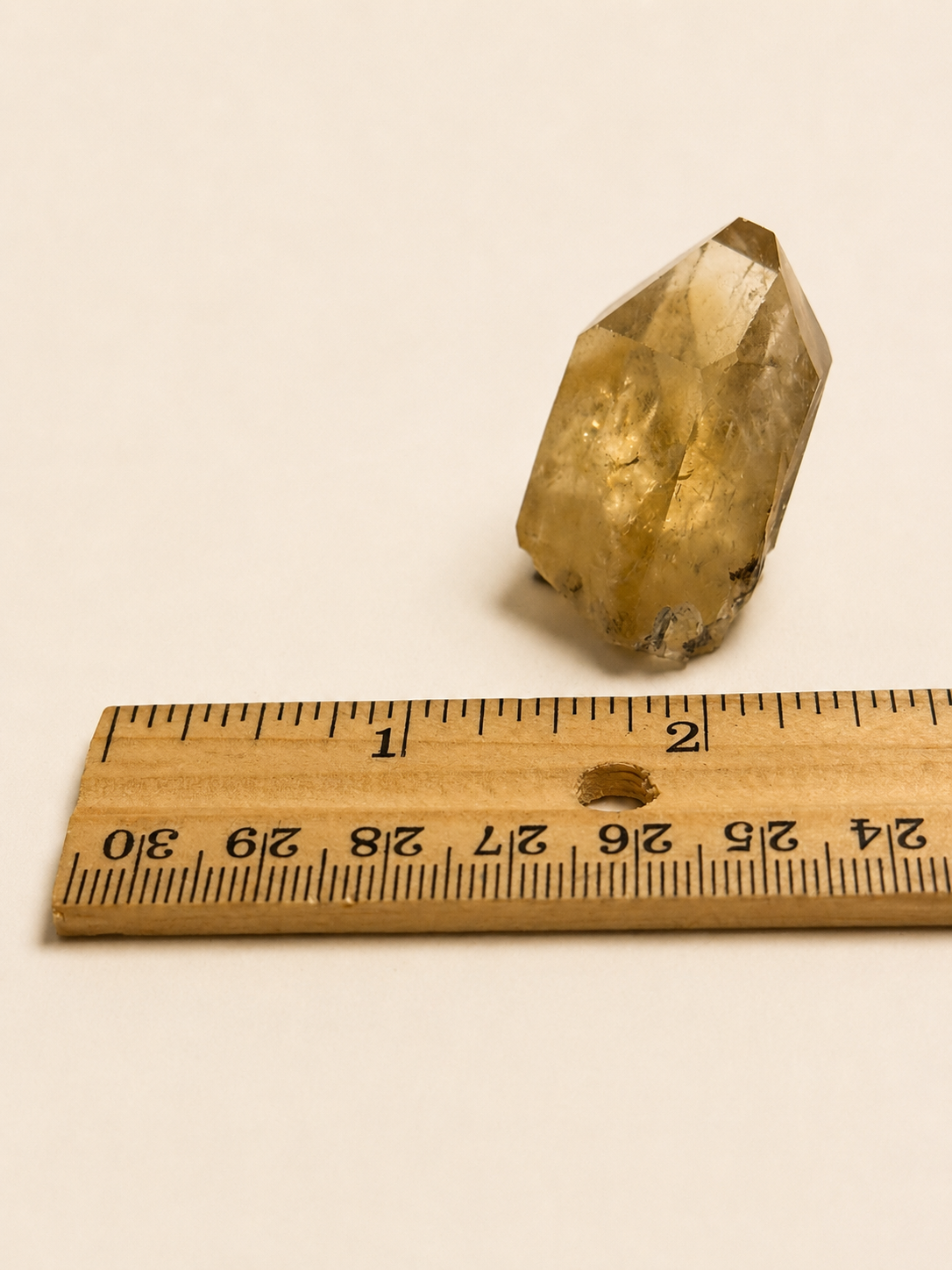 A small natural crystal or quartz point shown next to a wooden ruler on a plain off-white background, with the ruler indicating its approximate size.