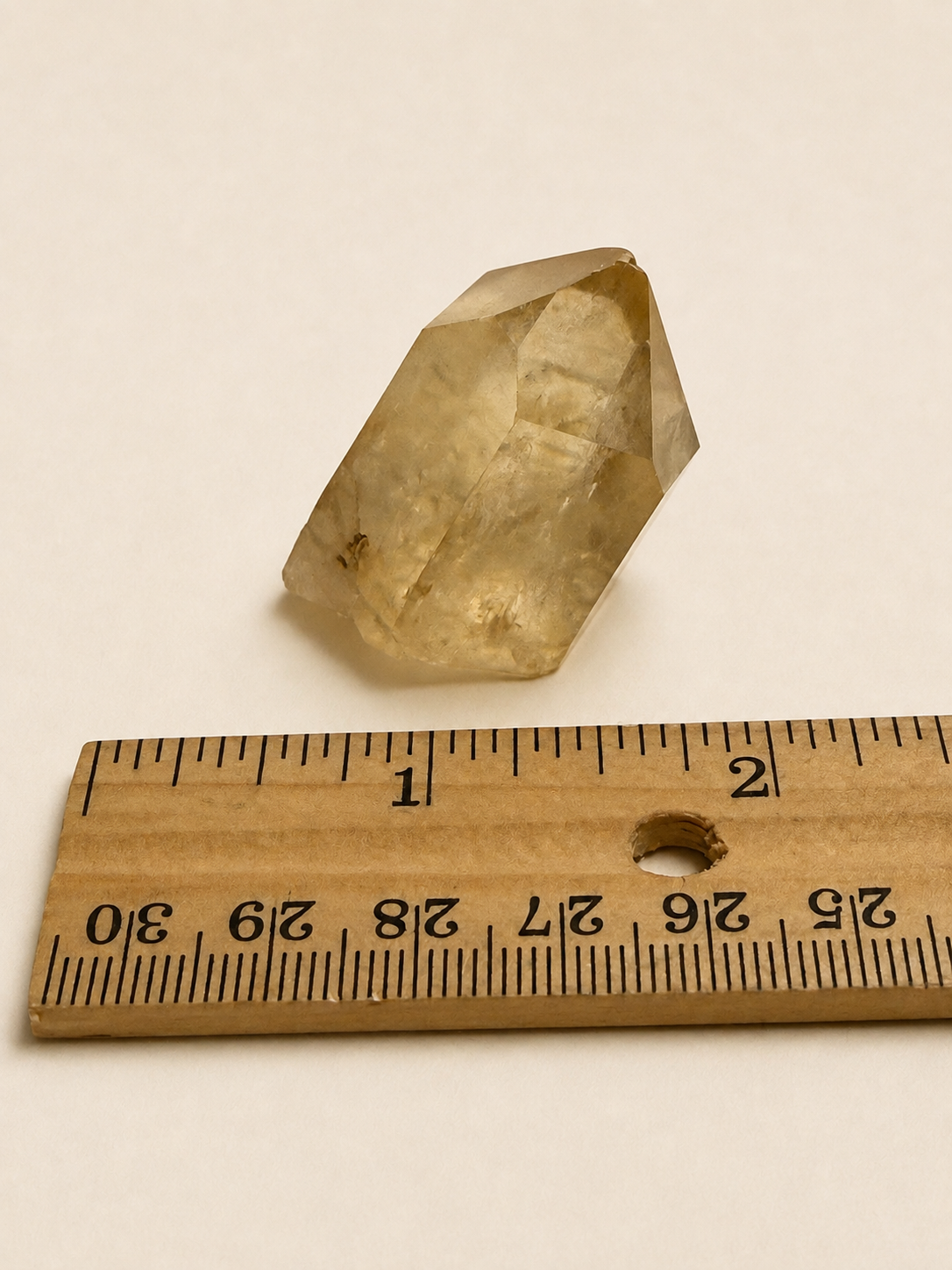 A small translucent pale yellow crystal or stone shown next to a wooden ruler for scale on a plain light background.