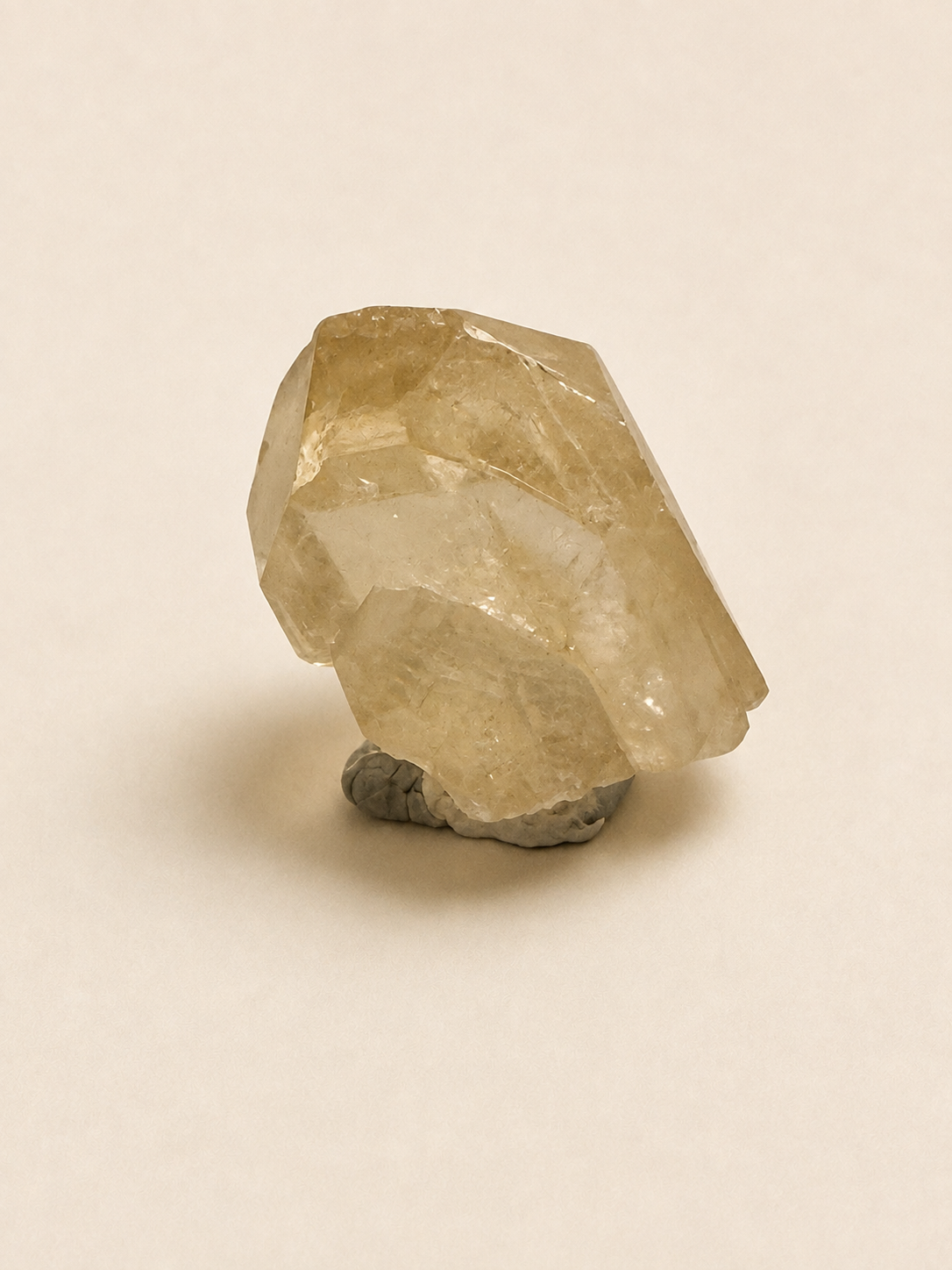A natural pale yellow quartz crystal cluster mounted on a small gray rock base, photographed against a plain warm off-white background.