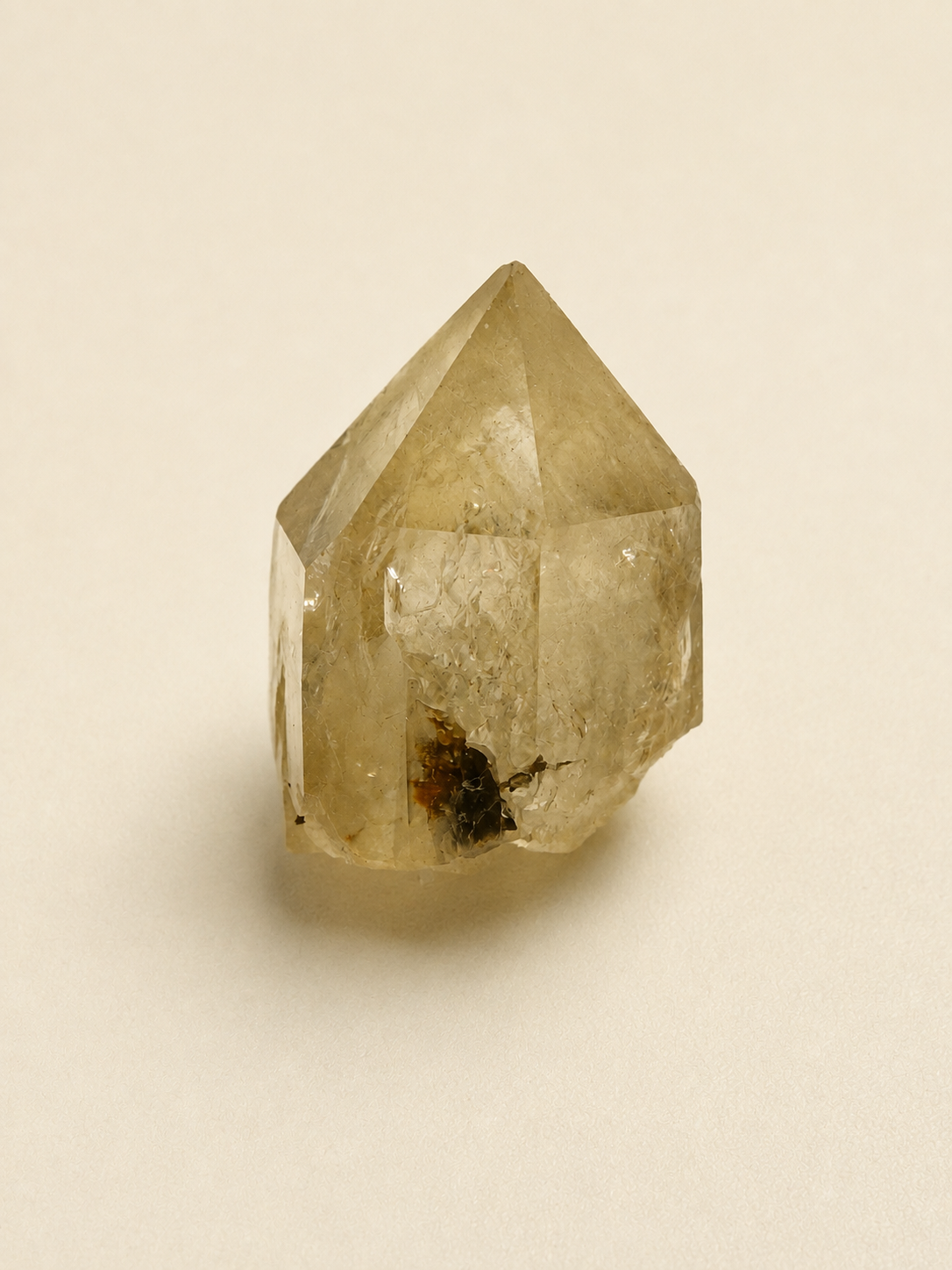 A natural citrine quartz crystal point with internal inclusions, shown on a plain beige background.