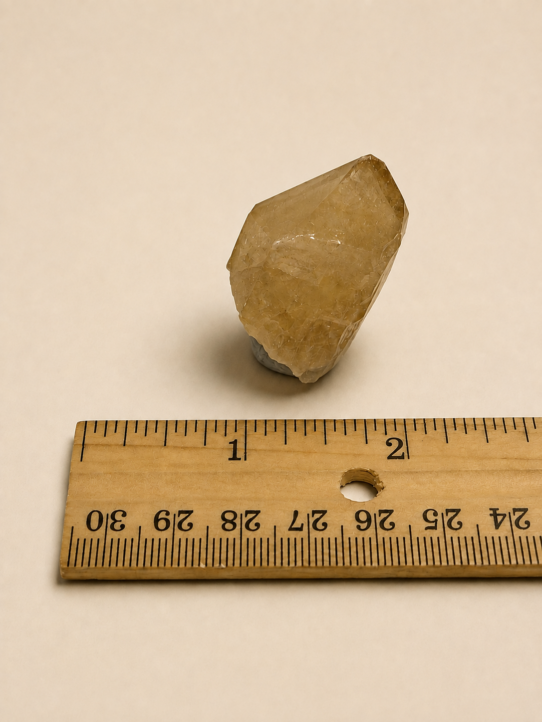 A small translucent pale yellow crystal or stone placed above a wooden ruler on a plain light beige background.