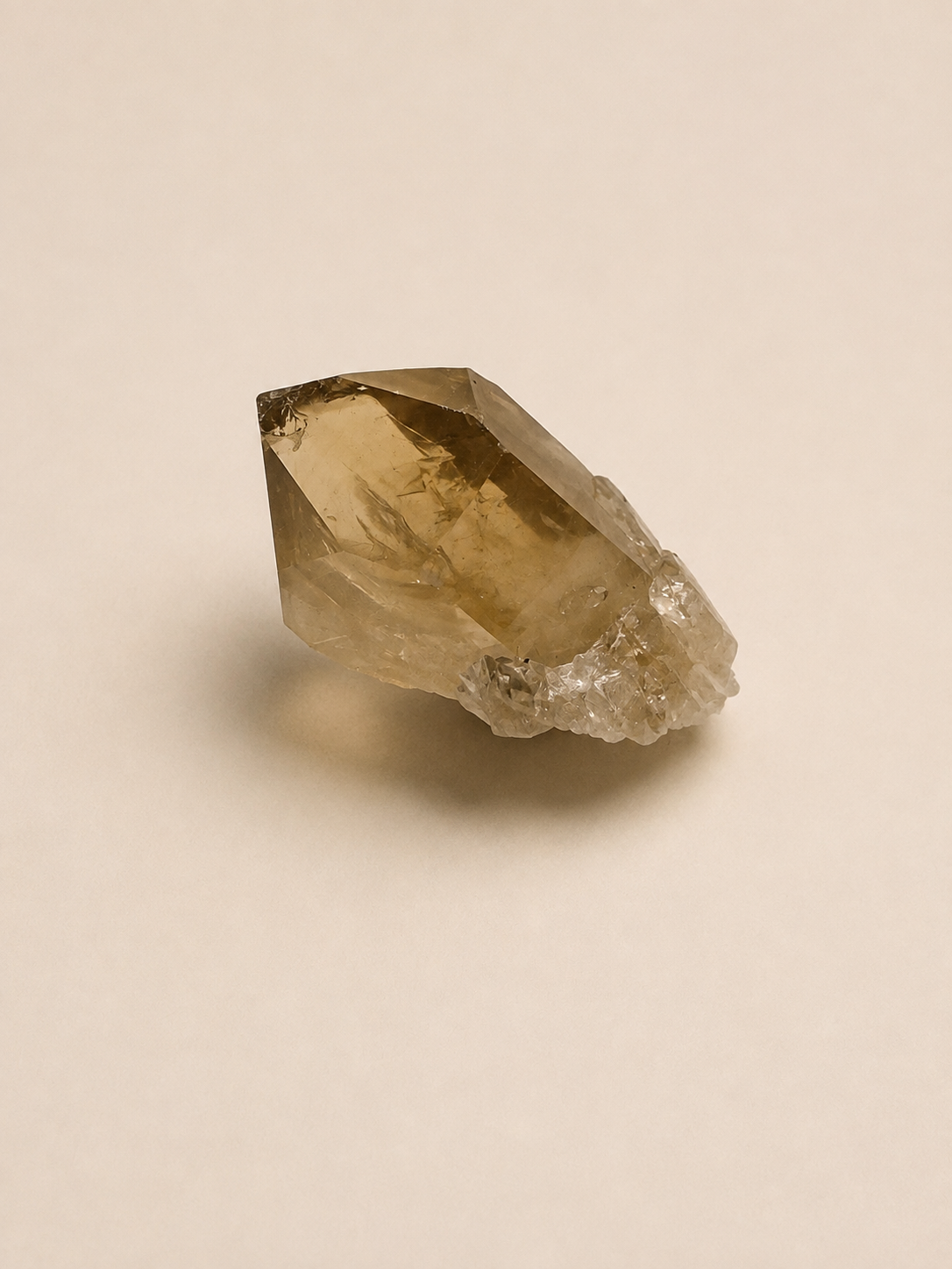 A natural smoky quartz crystal cluster with a rough, textured matrix base, photographed on a solid, warm beige background.