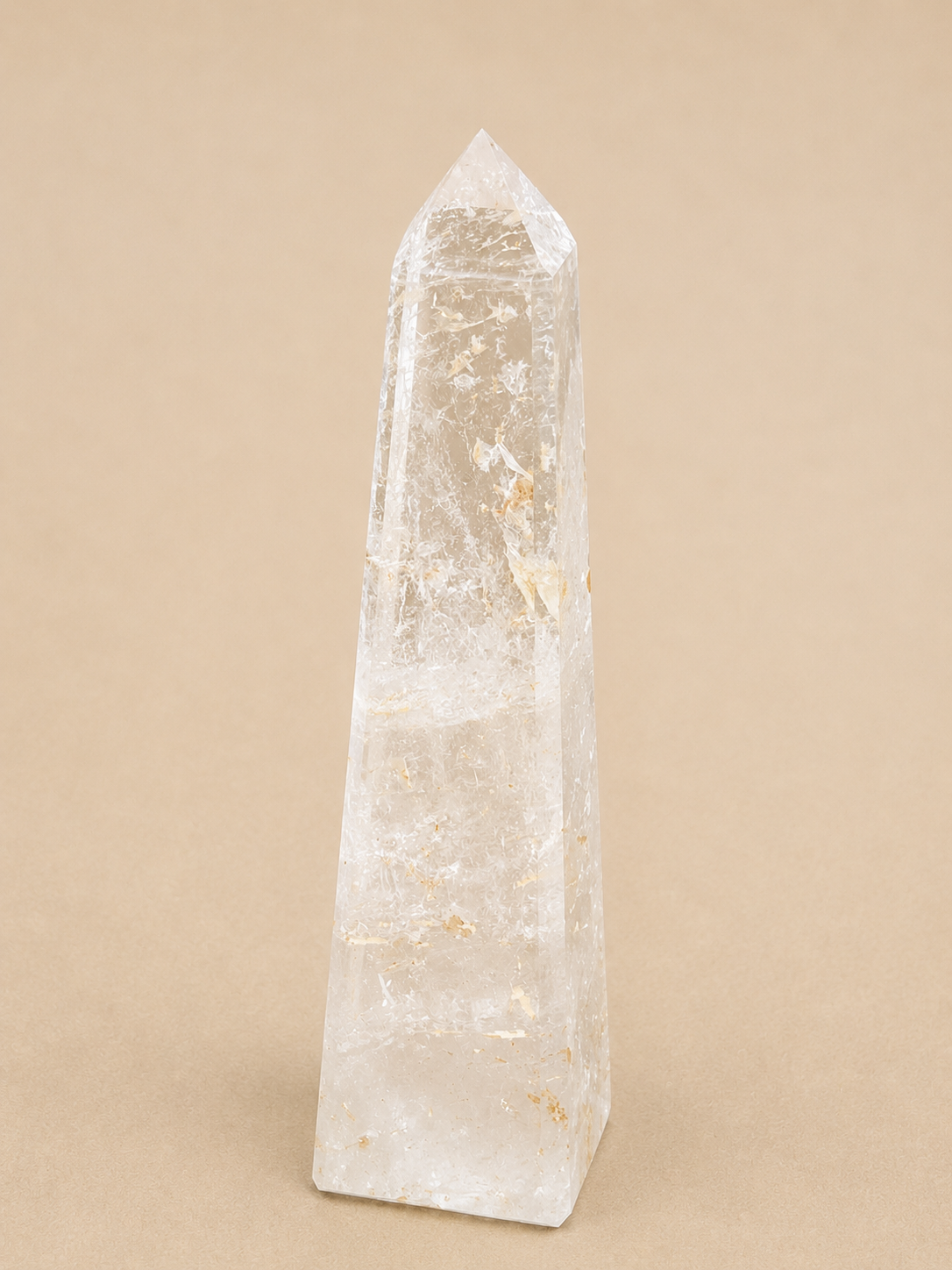A natural clear quartz crystal tower with a pointed tip, standing upright on a solid beige background.