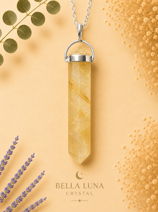 A yellow crystal point pendant necklace with a silver metal cap and chain, displayed on a warm peach background with decorative dried flowers and greenery. The brand name 'BELLA LUNA CRYSTAL' is printed at the bottom.
