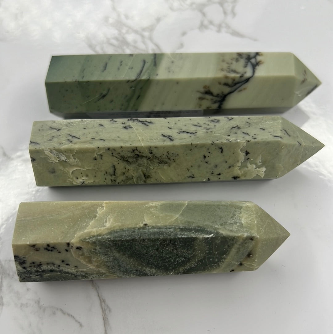 Three different angles of a green pyroxene crystal with dendritic inclusions, resembling a tower shape, placed on a marble surface.