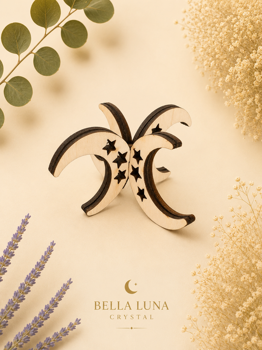 A crescent moon and star crystal pendant by Bella Luna Crystal, styled on a warm cream background with dried flowers and green leaves.