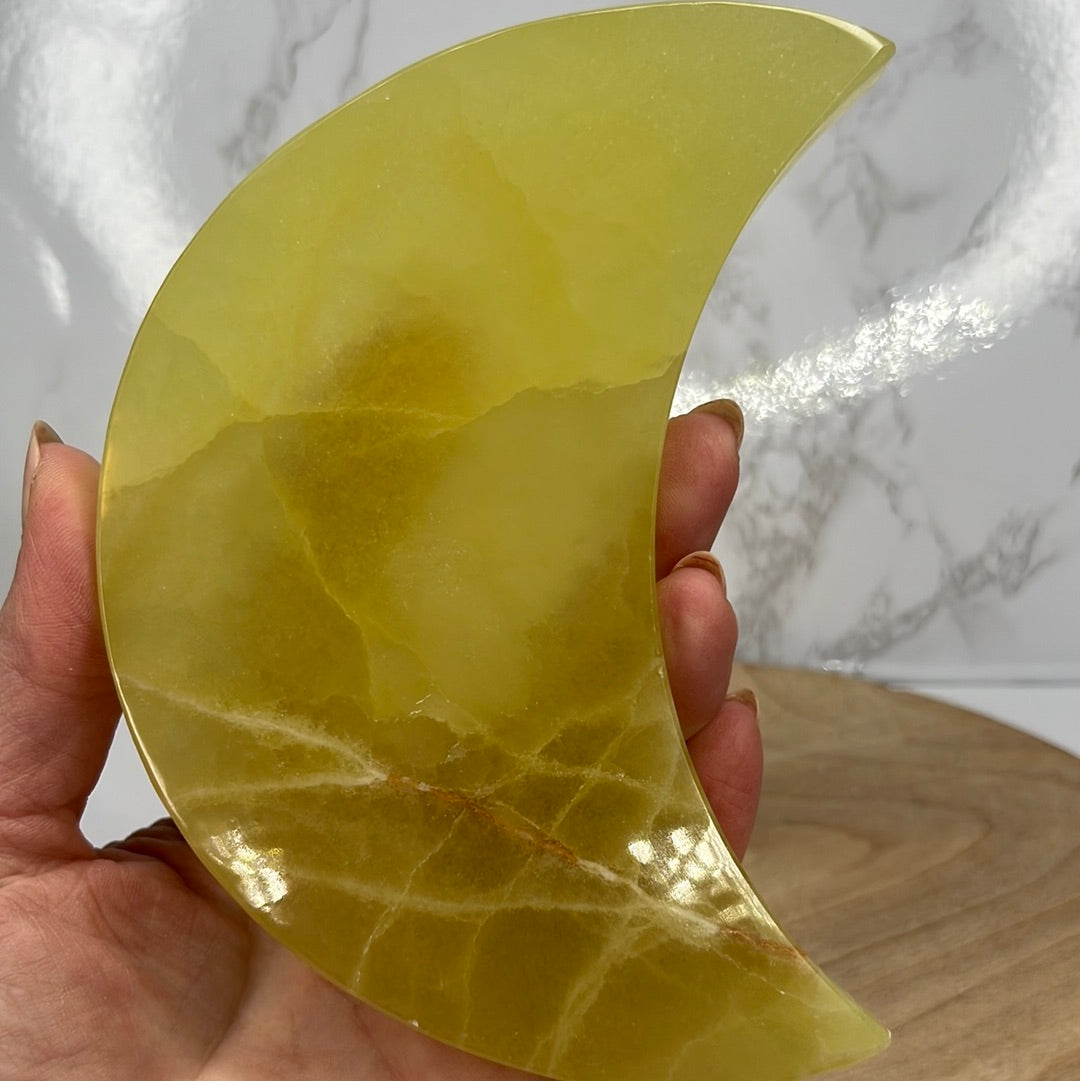 A hand holding a lemon yellow, moon-shaped piece of Lemon Calcite.