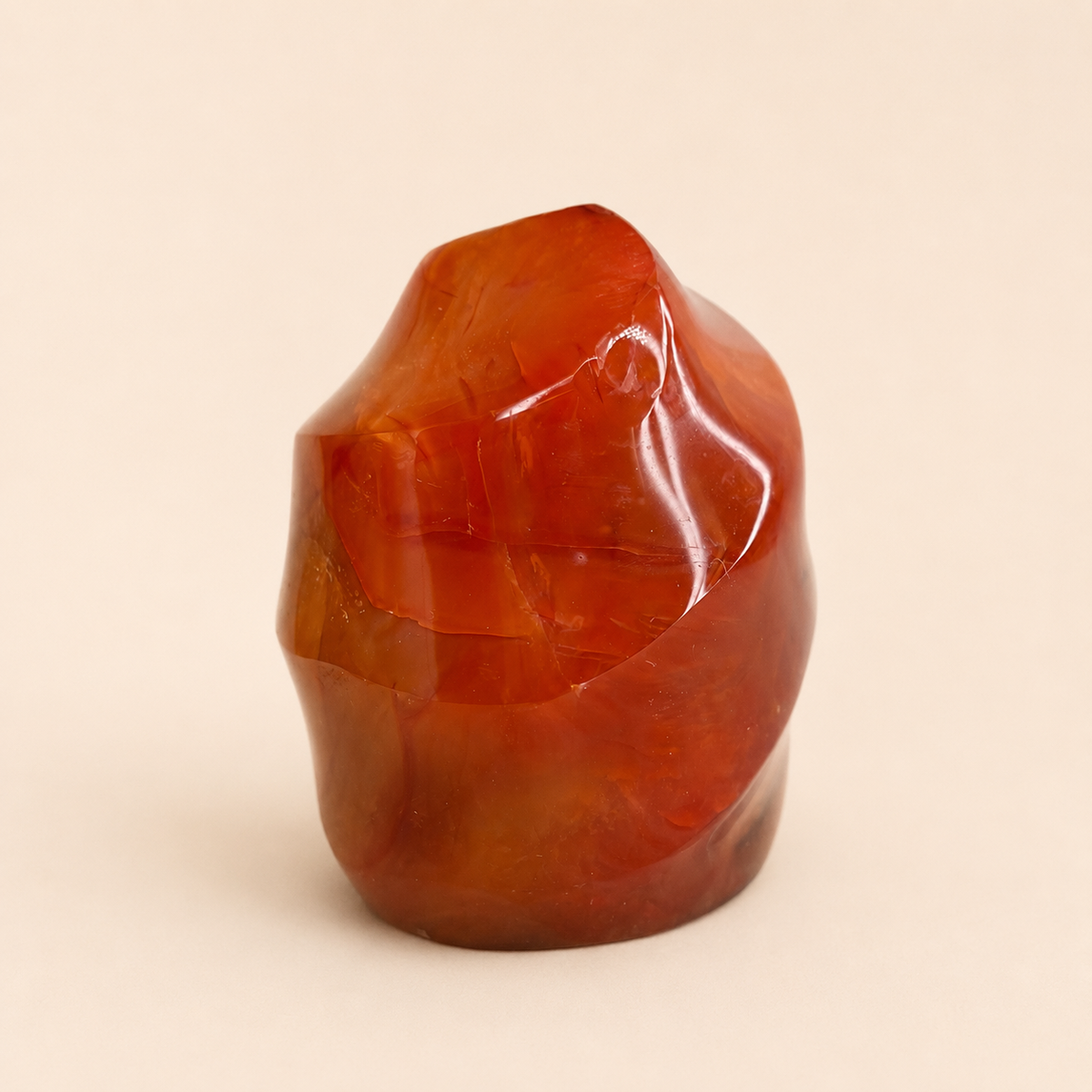 A polished, organic-shaped reddish-brown stone sculpture on a solid light beige background.