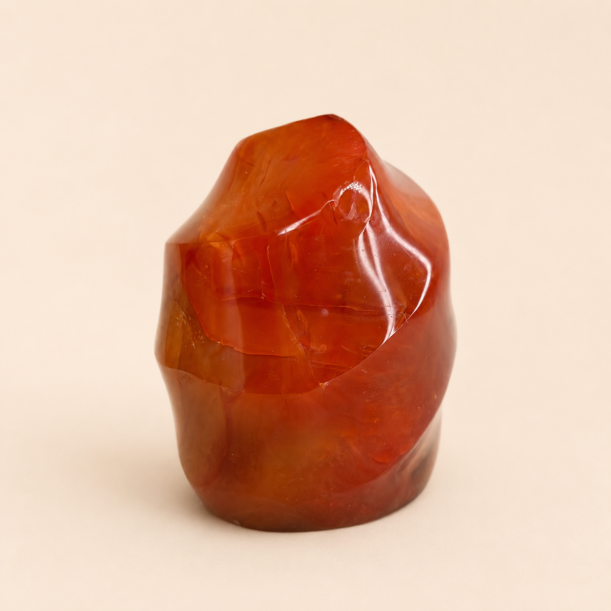 A polished, organic-shaped reddish-brown stone sculpture on a solid light beige background.