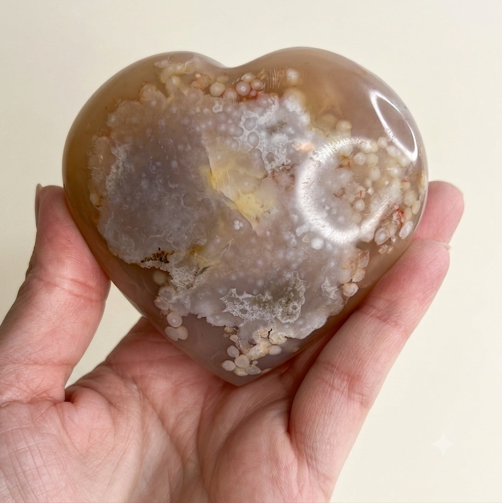 A heart-shaped polished agate stone held in a person's hand against a plain light background.