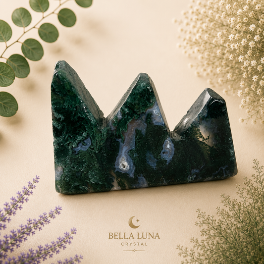 A three-pointed crystal tower with a dark green and blue marbled pattern, styled on a beige background with dried flowers and greenery, featuring the Bella Luna Crystal brand logo at the bottom.