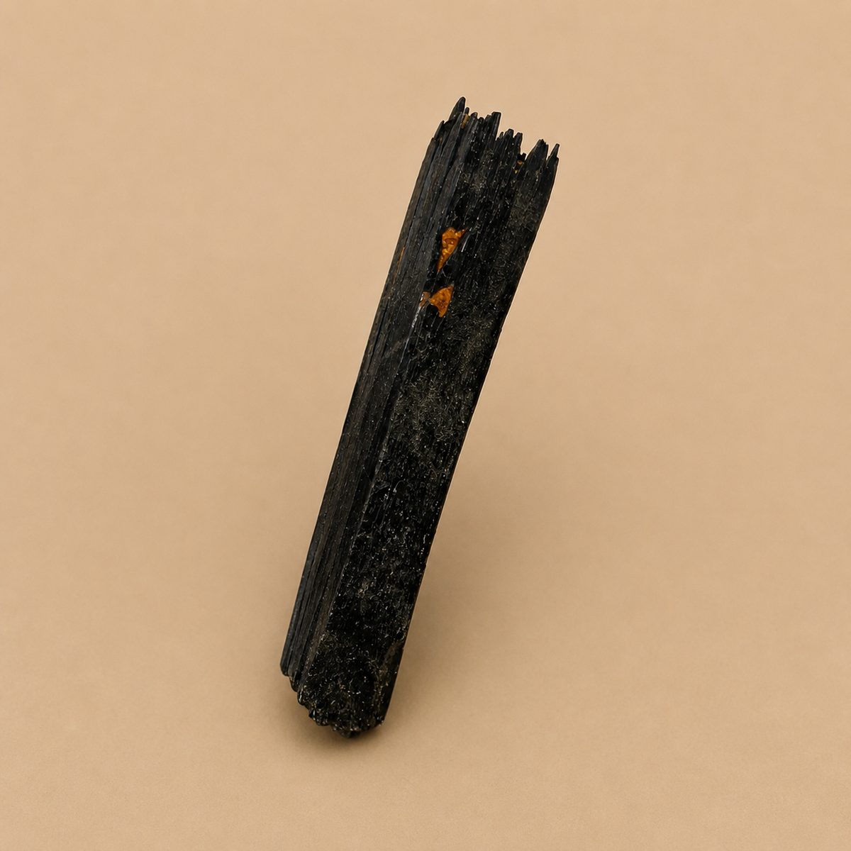 A single dark, textured mineral or stone specimen with jagged edges and small orange inclusions, photographed upright on a plain warm beige background.