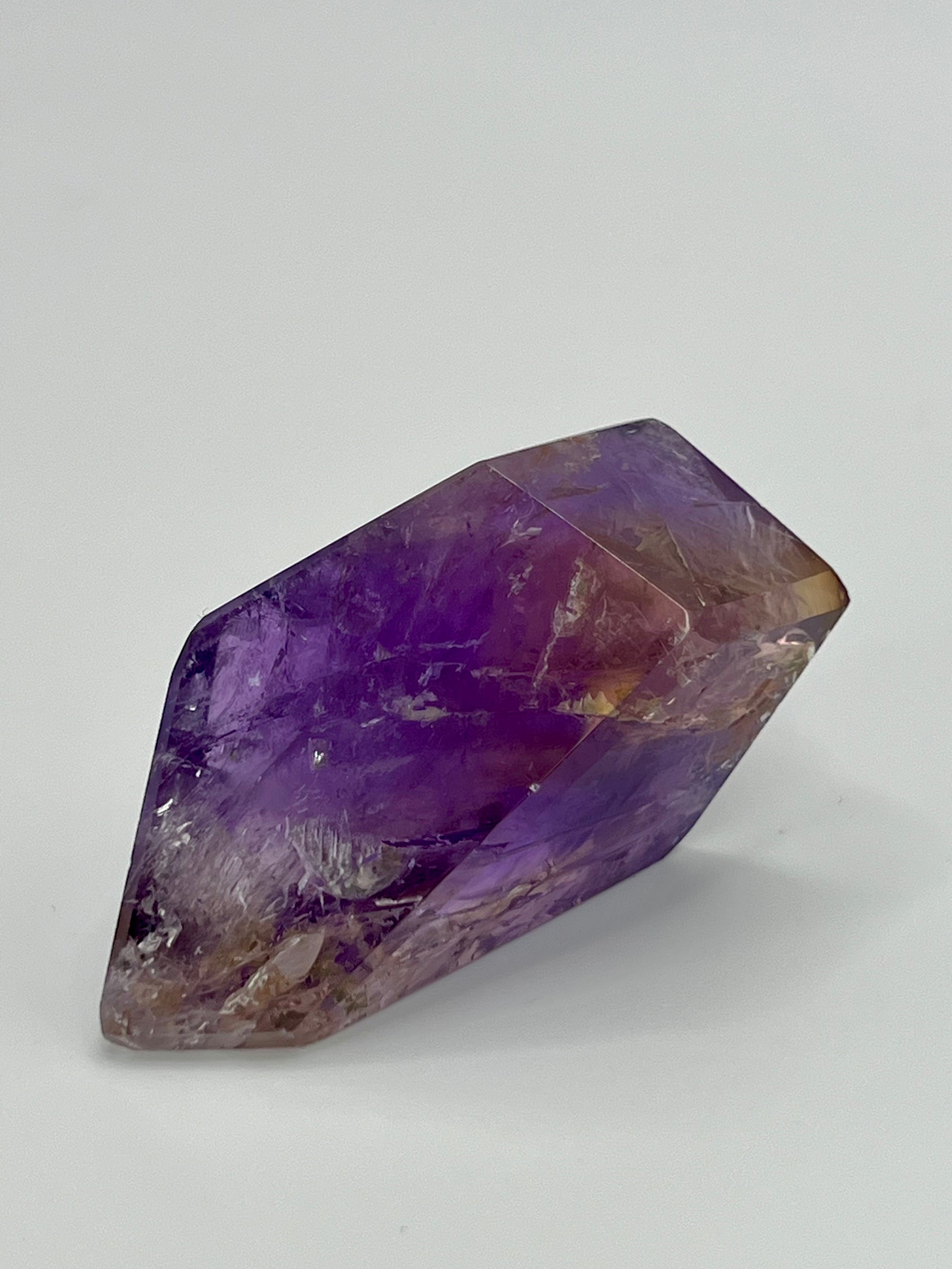 A polished ametrine crystal with a dual-color appearance, blending purple and yellow hues, placed on a white background.