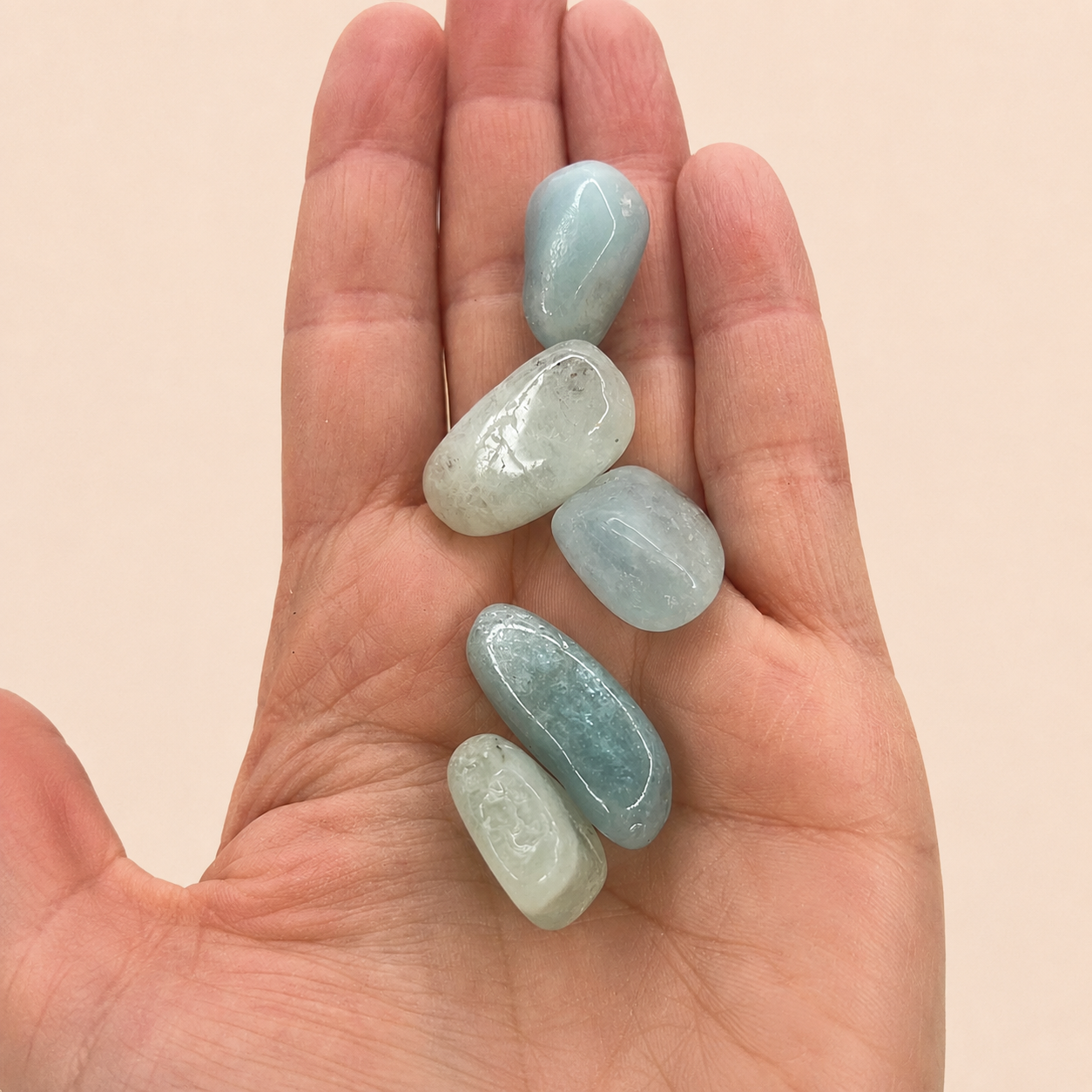 Five polished light blue tumbled stones resting on an open human hand against a soft beige background.