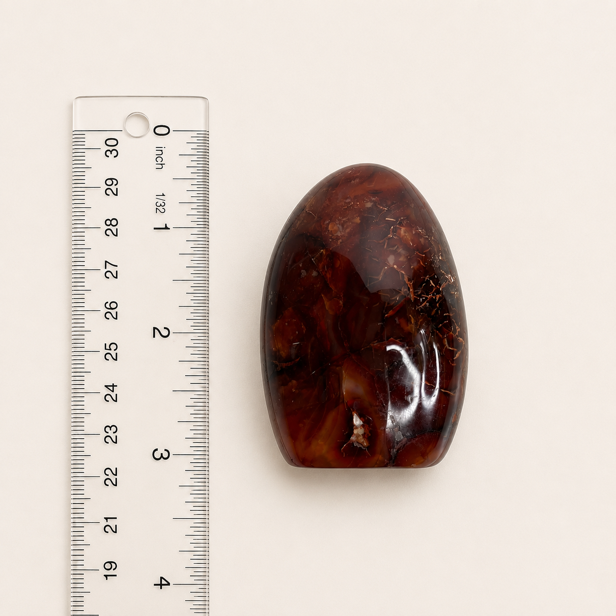 A polished oval-shaped brown stone or agate cabochon displayed next to a clear plastic ruler with inch markings on a light beige background.