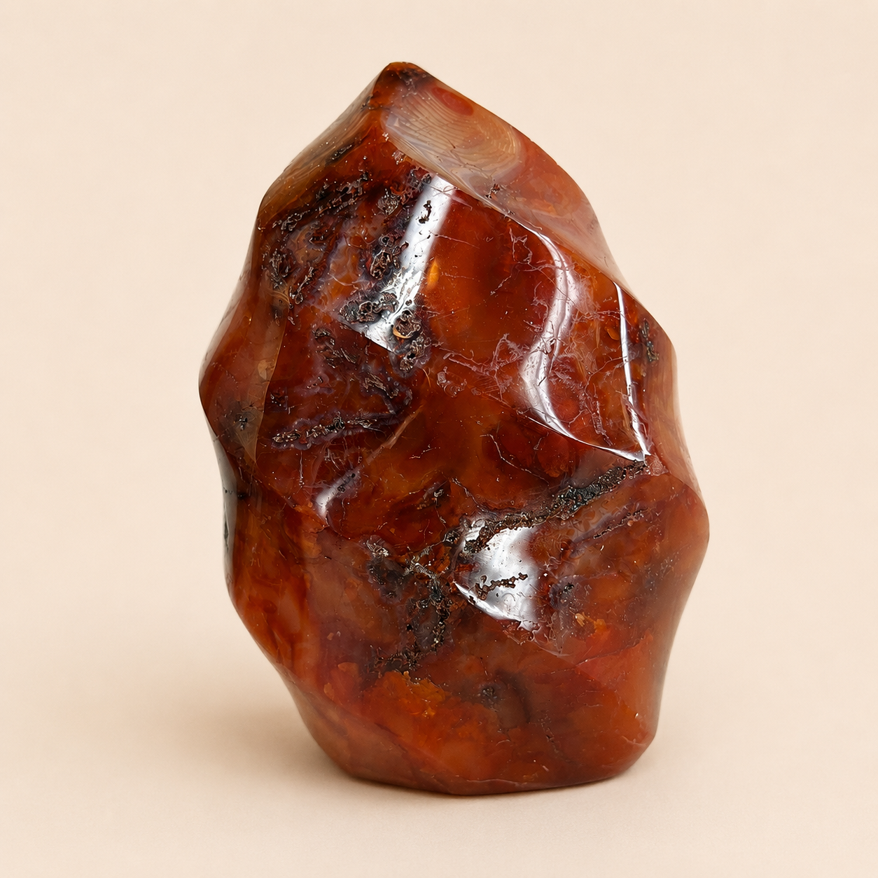 A polished rough stone sculpture in warm amber-brown tones with glossy highlights and dark inclusions, photographed against a plain warm beige background.