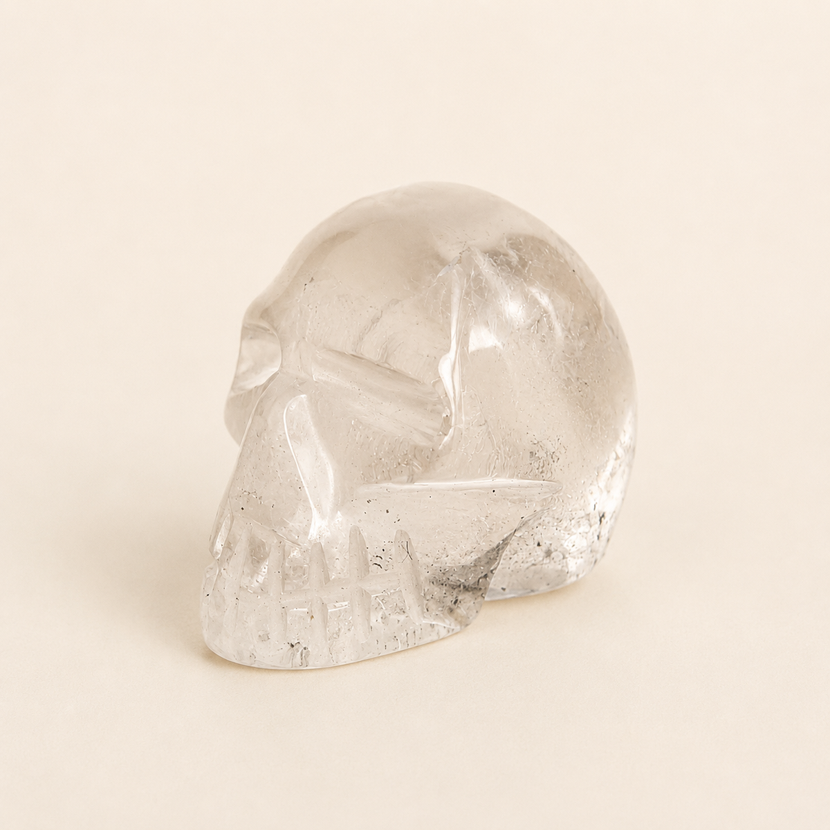 A clear glass or crystal skull figurine with embedded dark flecks, set against a solid, warm off-white background.