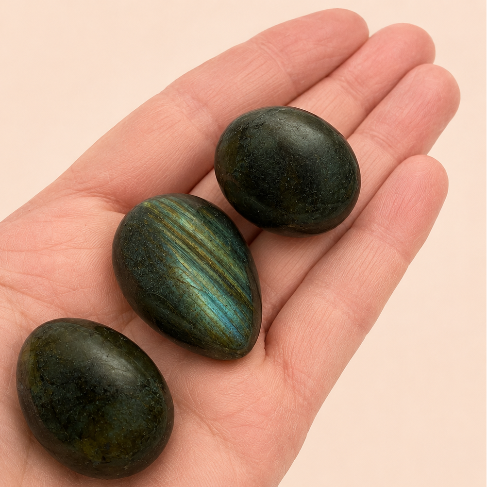 Three polished labradorite stones resting on an open hand against a soft beige background.