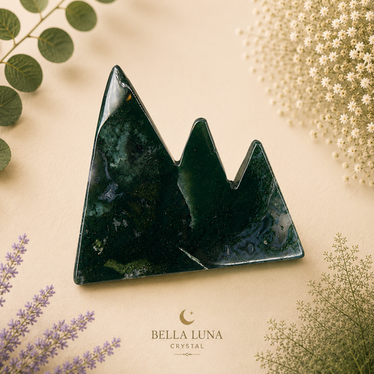 A triangular mountain-shaped crystal pendant made of dark green marbled stone, displayed on a beige background with decorative botanical elements and the Bella Luna Crystal logo at the bottom.