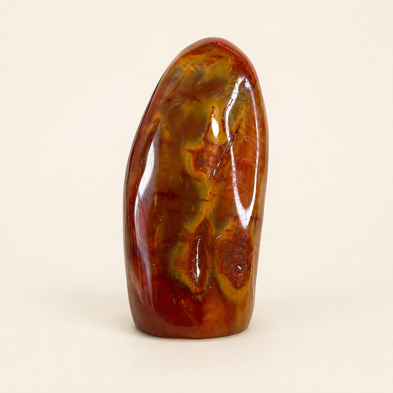 A polished natural stone sculpture with swirling patterns of amber brown, reddish orange, and olive green, standing upright against a plain off-white background.
