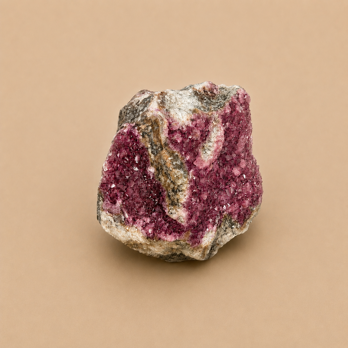 A raw mineral specimen featuring a magenta-pink crystal cluster on a rough, earthy gray and beige matrix, set against a solid tan background.