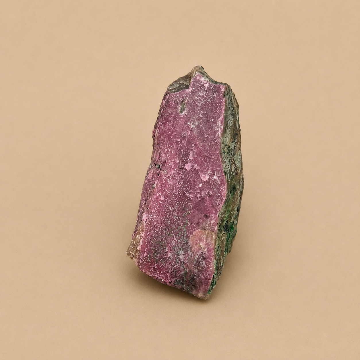 A raw mineral specimen showing a pinkish-purple matrix with green crystalline edges, photographed on a solid beige background.
