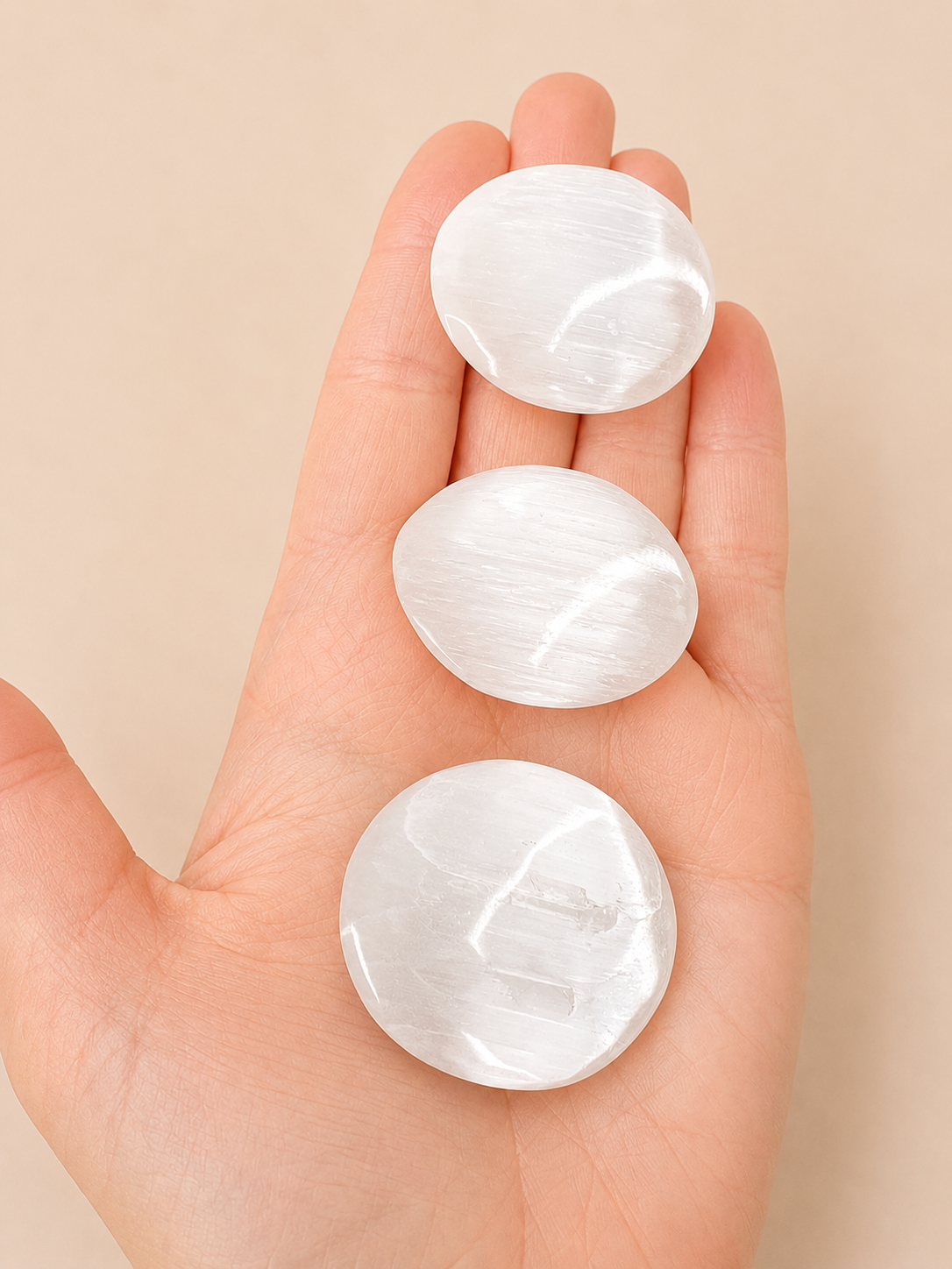 Three smooth, polished white oval stones resting on an open hand against a soft beige background.