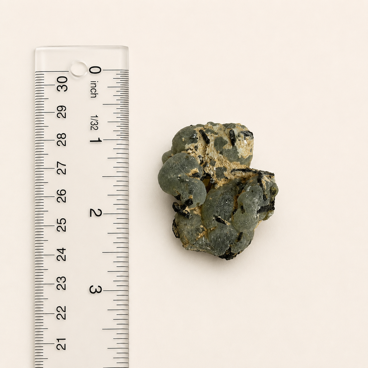 A small rough, translucent green-gray stone or mineral sample shown next to a clear plastic ruler on a plain off-white background.