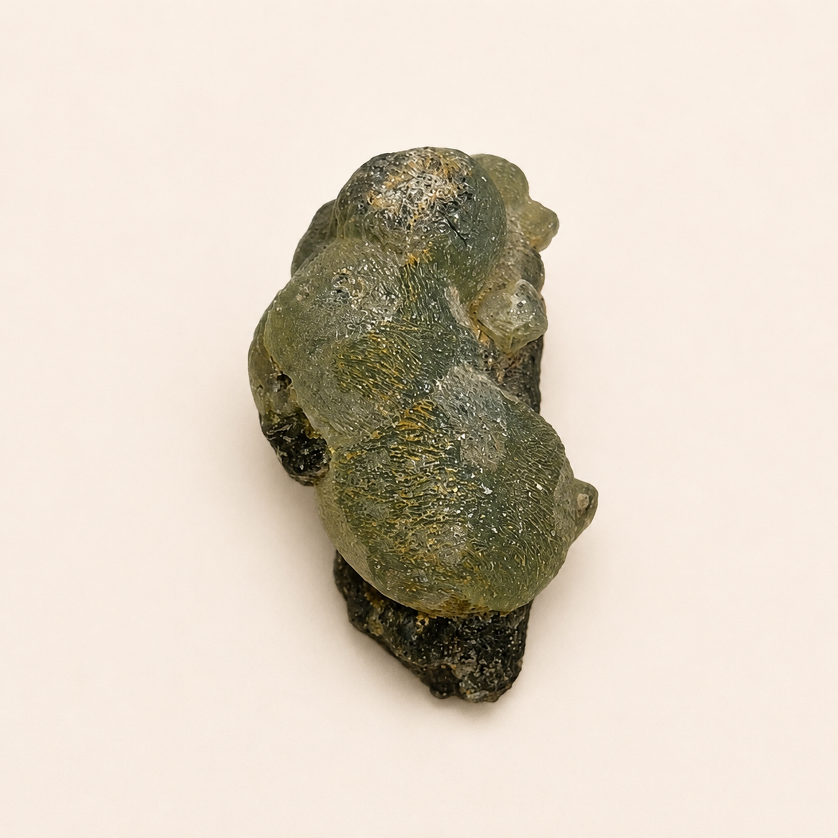 A rough, organic-shaped green stone or mineral specimen with a dark base, photographed on a plain light beige background.