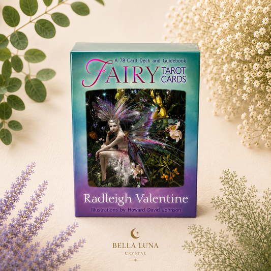 A boxed card deck and guidebook titled 'Fairy Tarot Cards' by Radleigh Valentine, photographed upright on a light cream surface with decorative green and white botanicals around it. The box has a teal-to-purple gradient cover with a fairy illustration in the center.