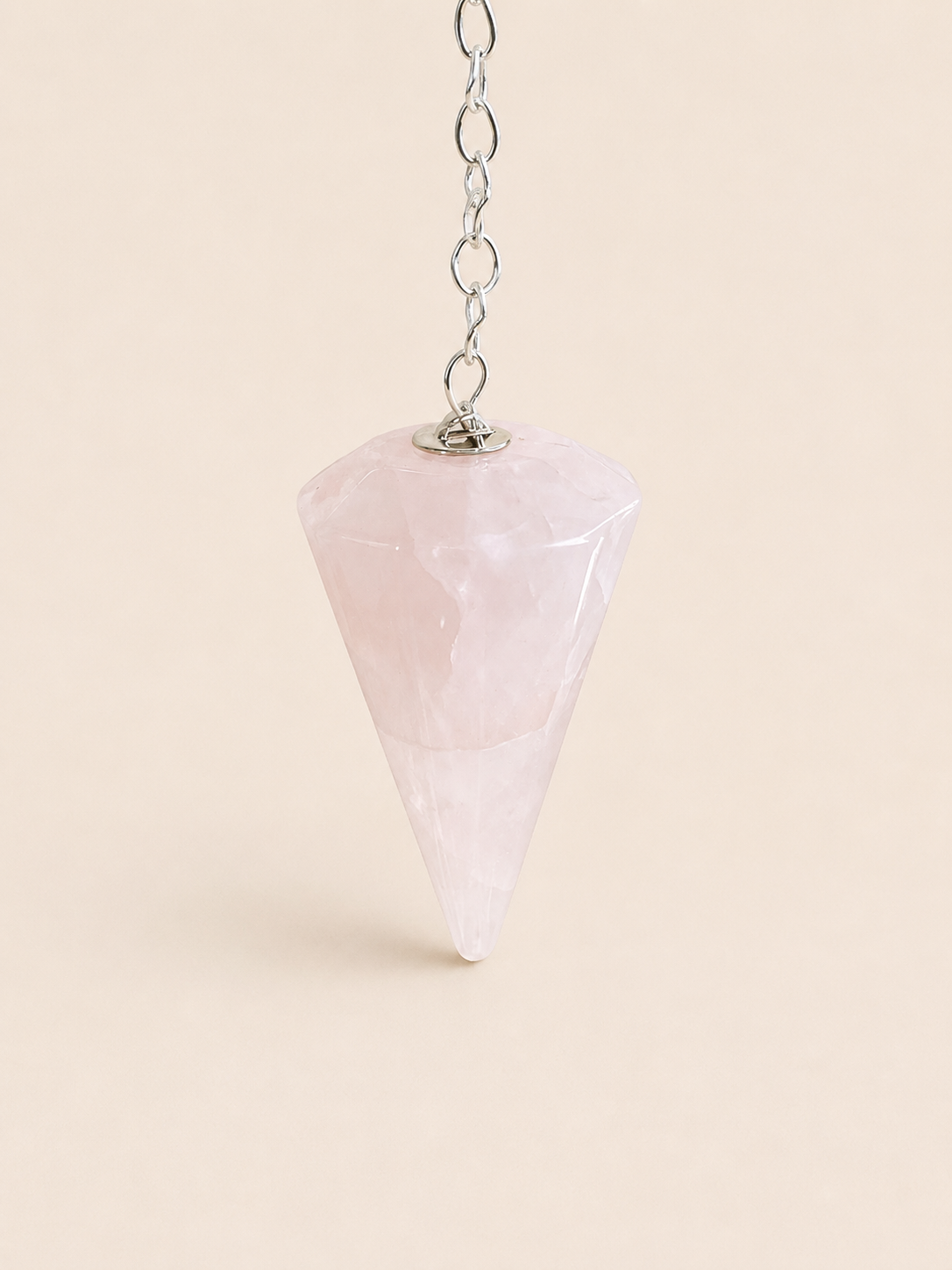 A faceted pink quartz crystal pointer hanging from a silver metal chain against a solid pale beige background.