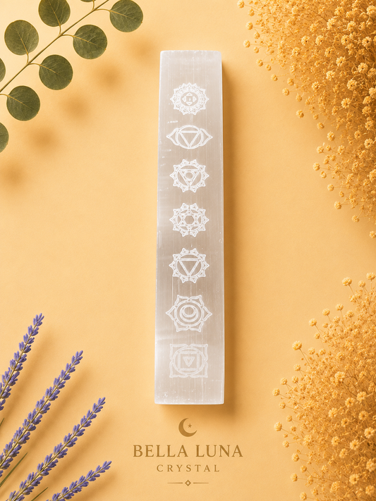 A vertical white crystal block featuring the seven chakras etched in white, displayed on a warm peach background with decorative dried flowers, lavender, and eucalyptus leaves. The brand name 'BELLA LUNA CRYSTAL' is printed at the bottom.