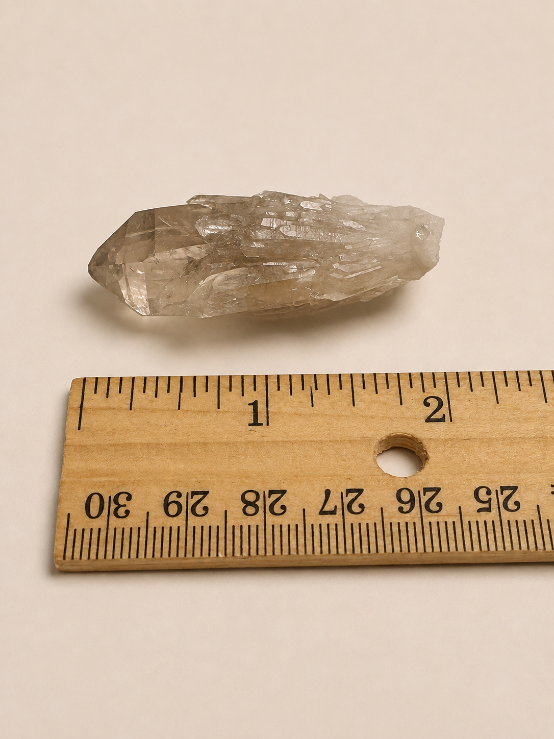 A small translucent smoky crystal or mineral specimen placed above a wooden ruler on a plain light beige background.