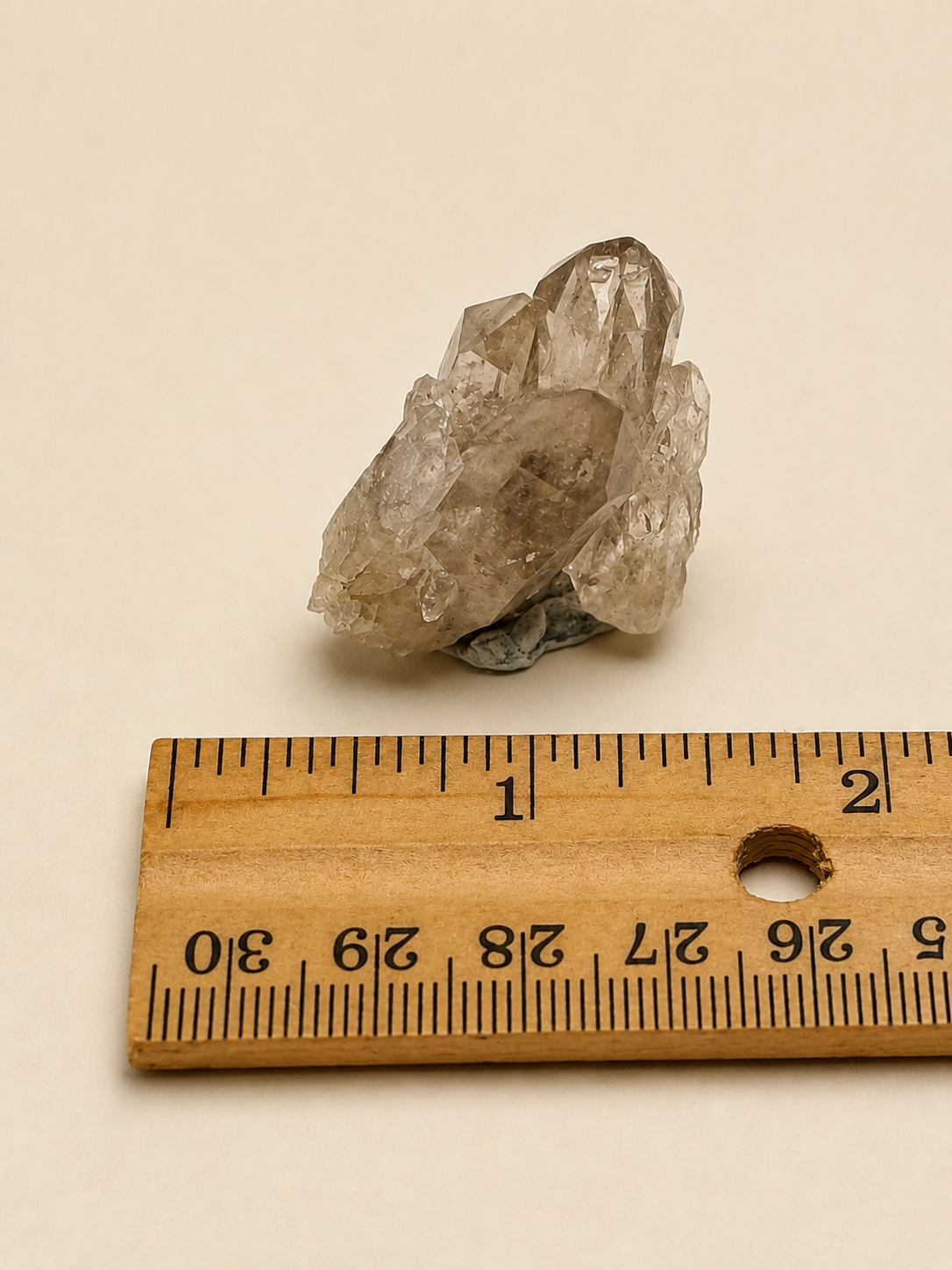 A raw, rough translucent crystal specimen shown above a wooden ruler on a plain beige background.