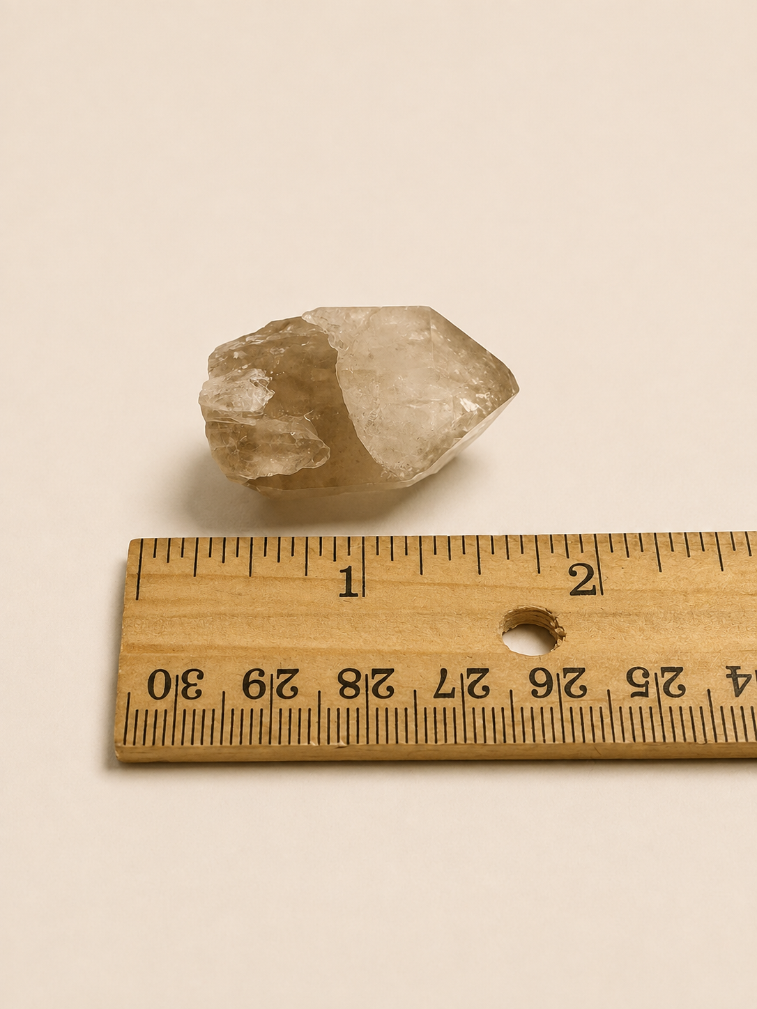 A small translucent pale crystal or stone placed above a wooden ruler on a plain warm beige background.