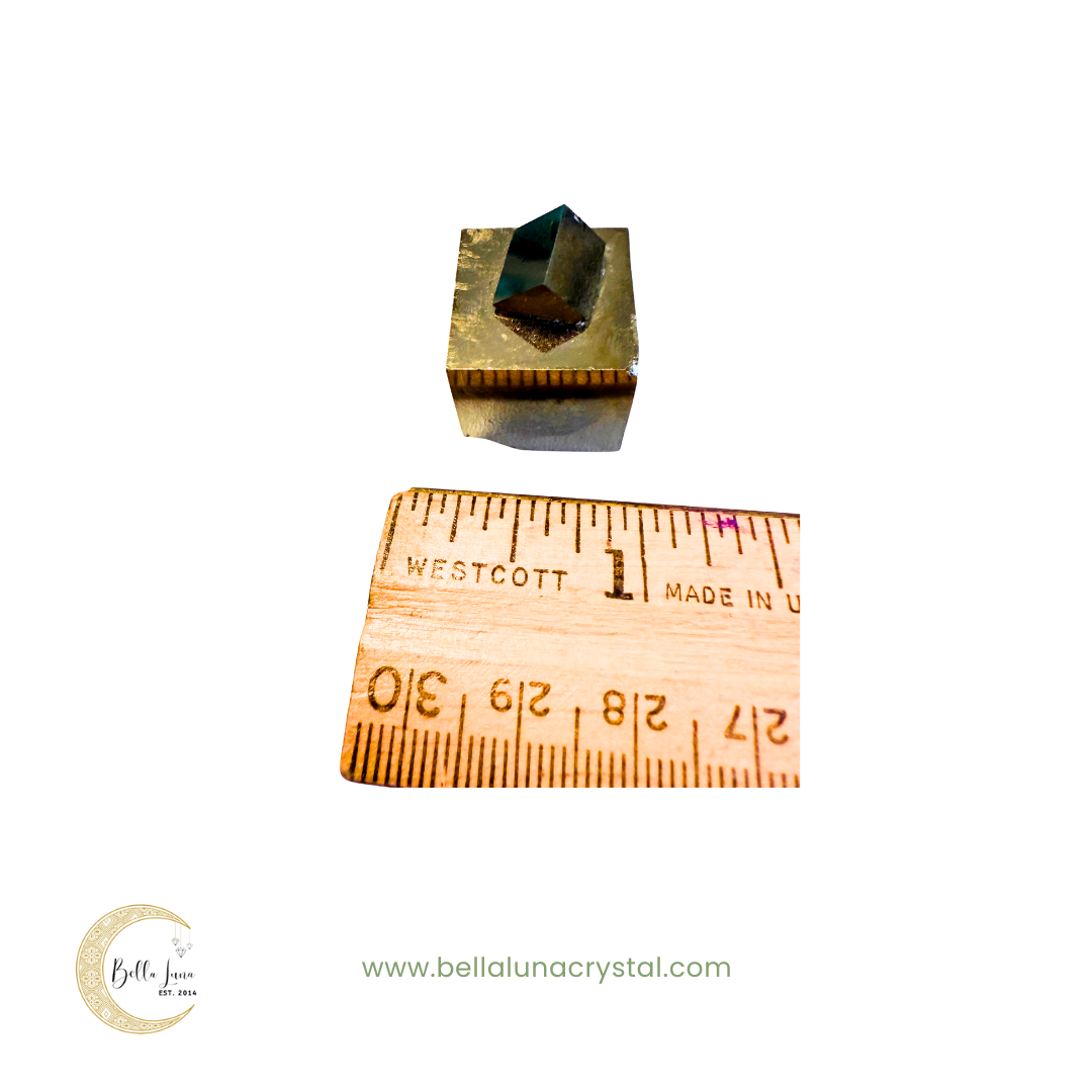 pyrite crystal with a ruler for scale on a white background, featuring Bella Luna Crystal logo.